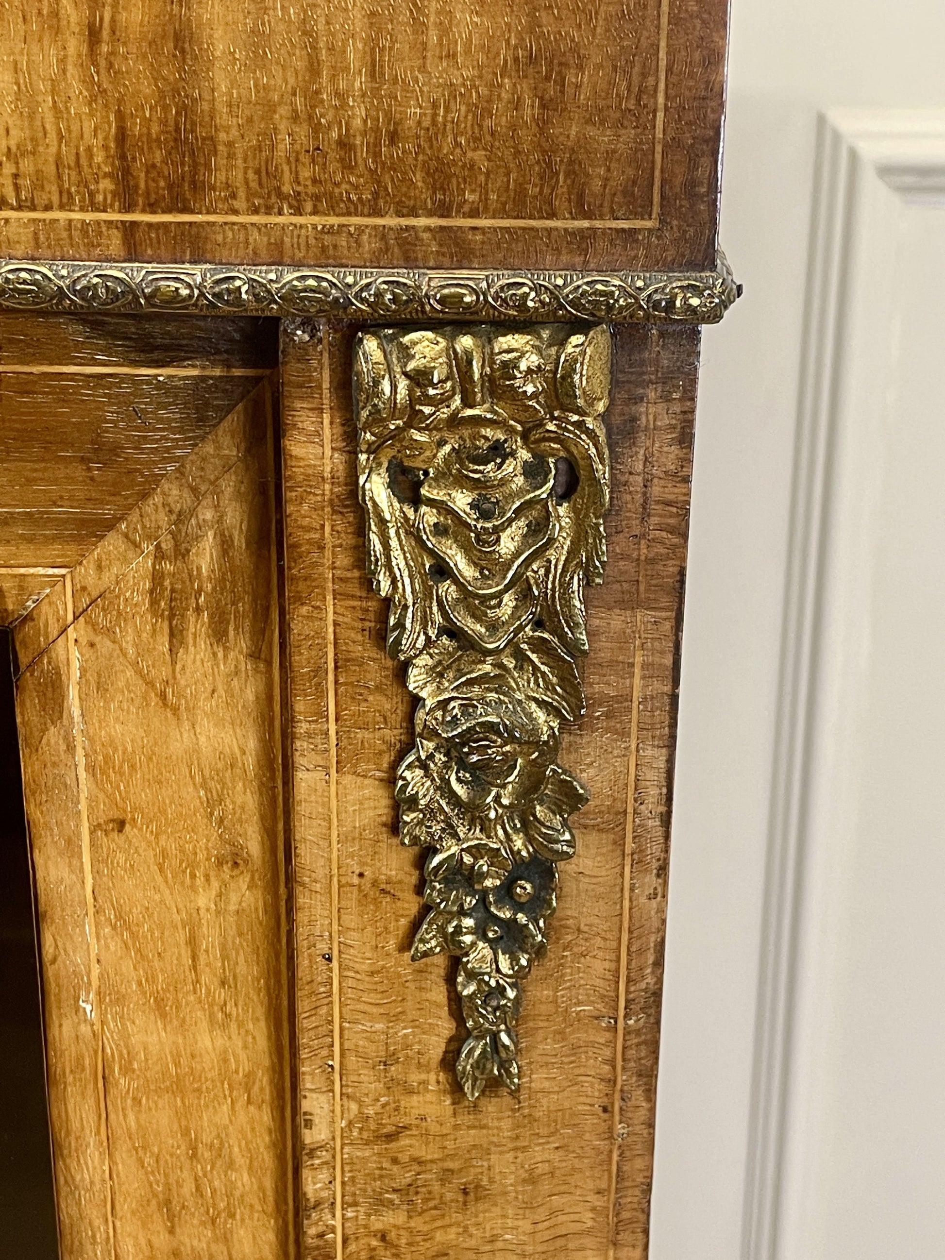 Wooden cabinet with ornate gold detailing on a white wall
