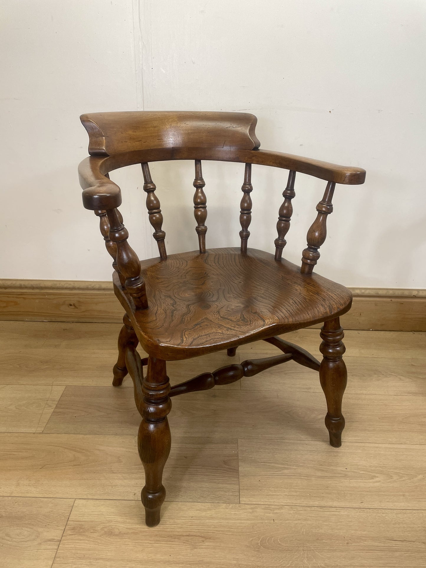 Wooden chair with armrests on a wooden floor against a white wall