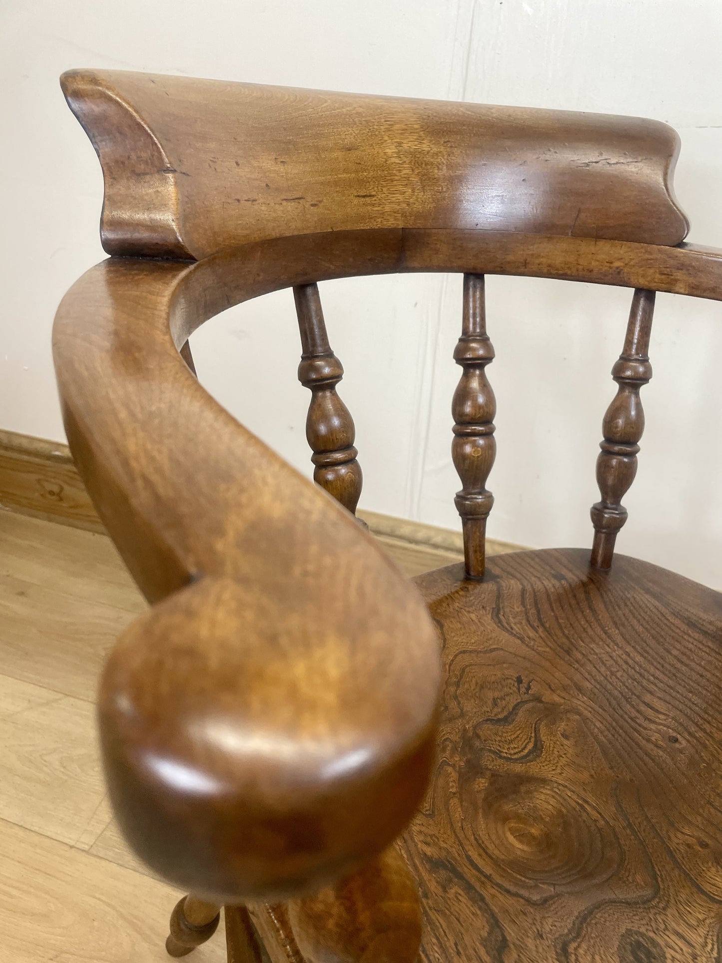 Close-up of a wooden chair with curved backrest and armrests on a light wood floor.
