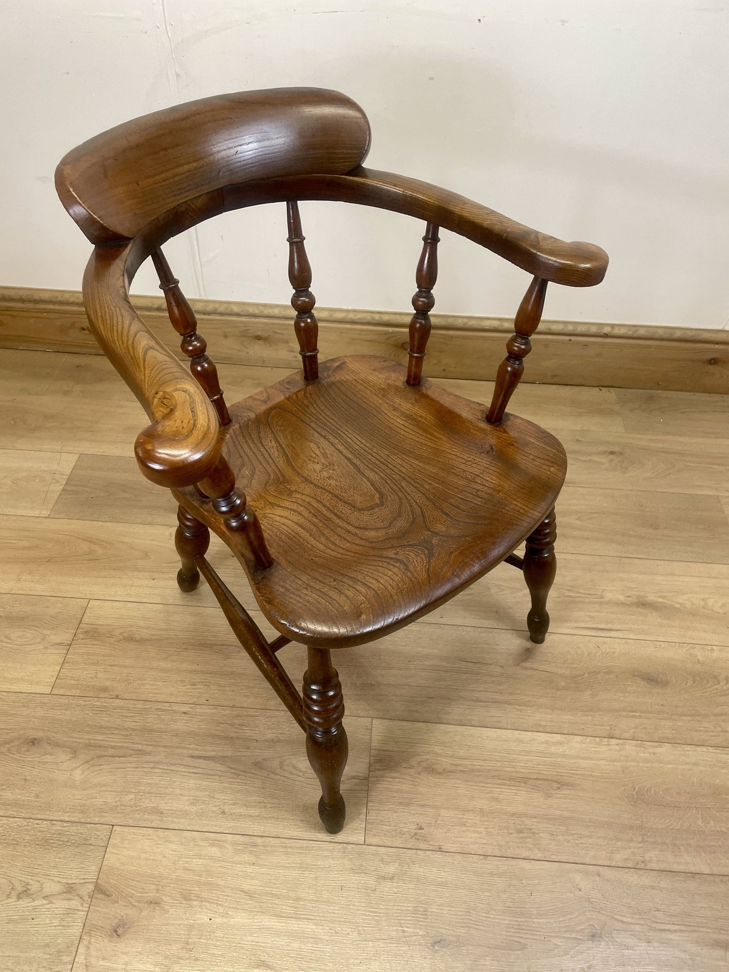Wooden chair with curved backrest and armrests on a wooden floor.
