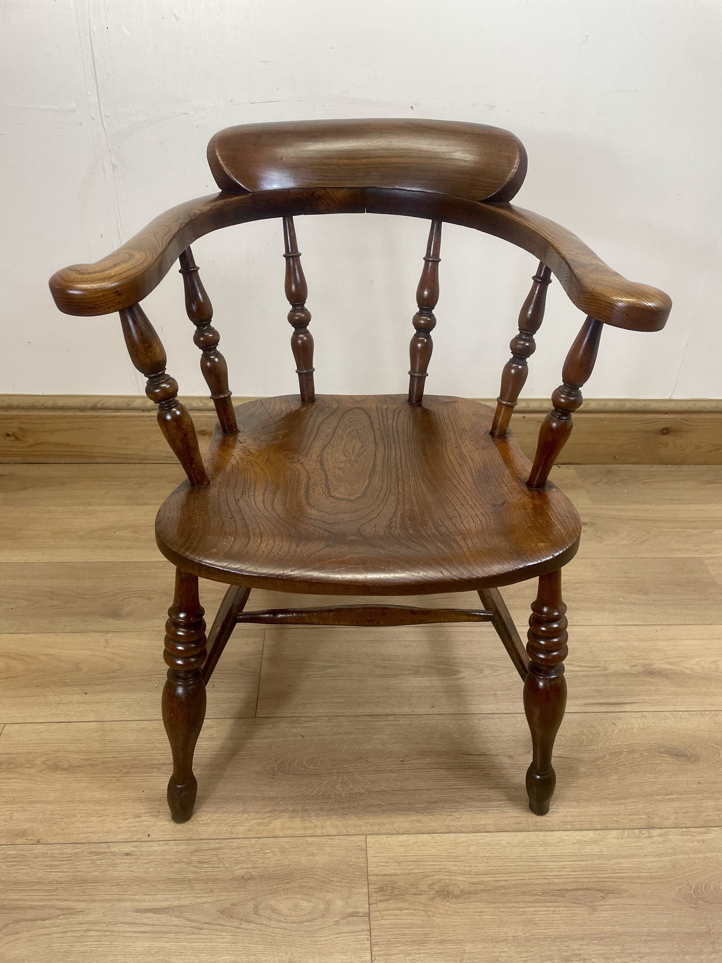 Wooden chair with spindle back and armrests on a wooden floor.