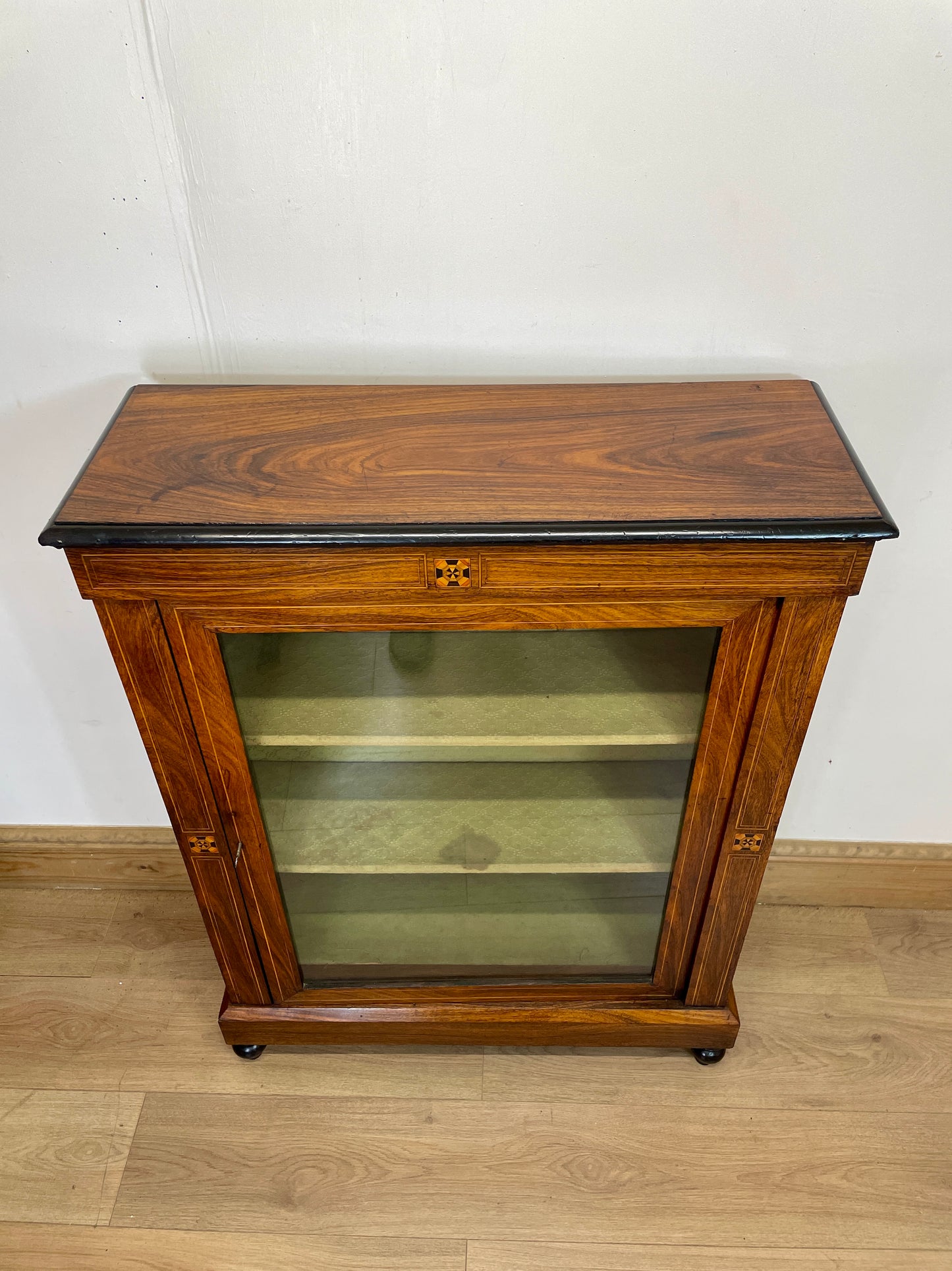 Wooden display cabinet with glass door on a wooden floor.
