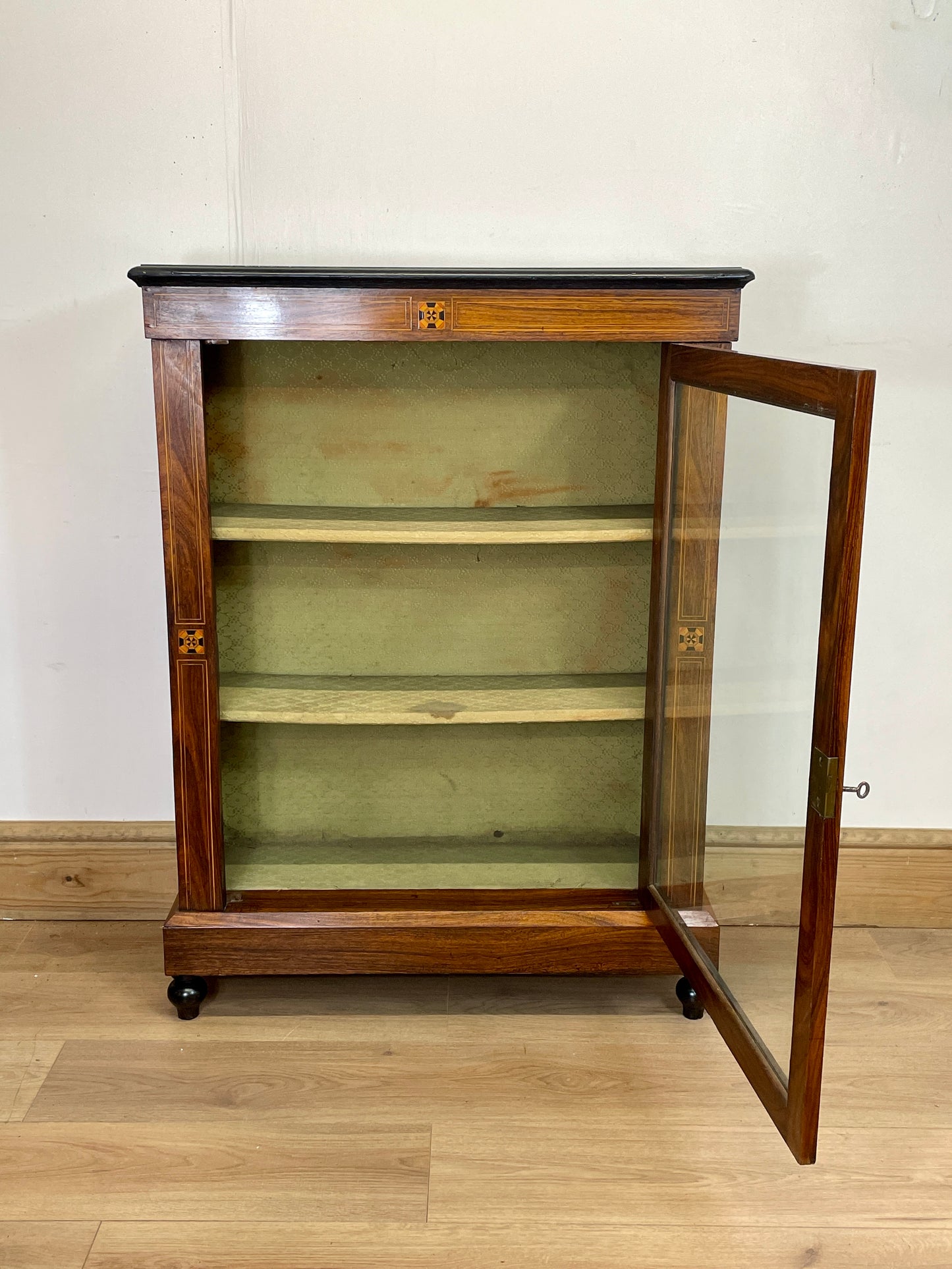 Wooden display cabinet with glass door on a wooden floor.