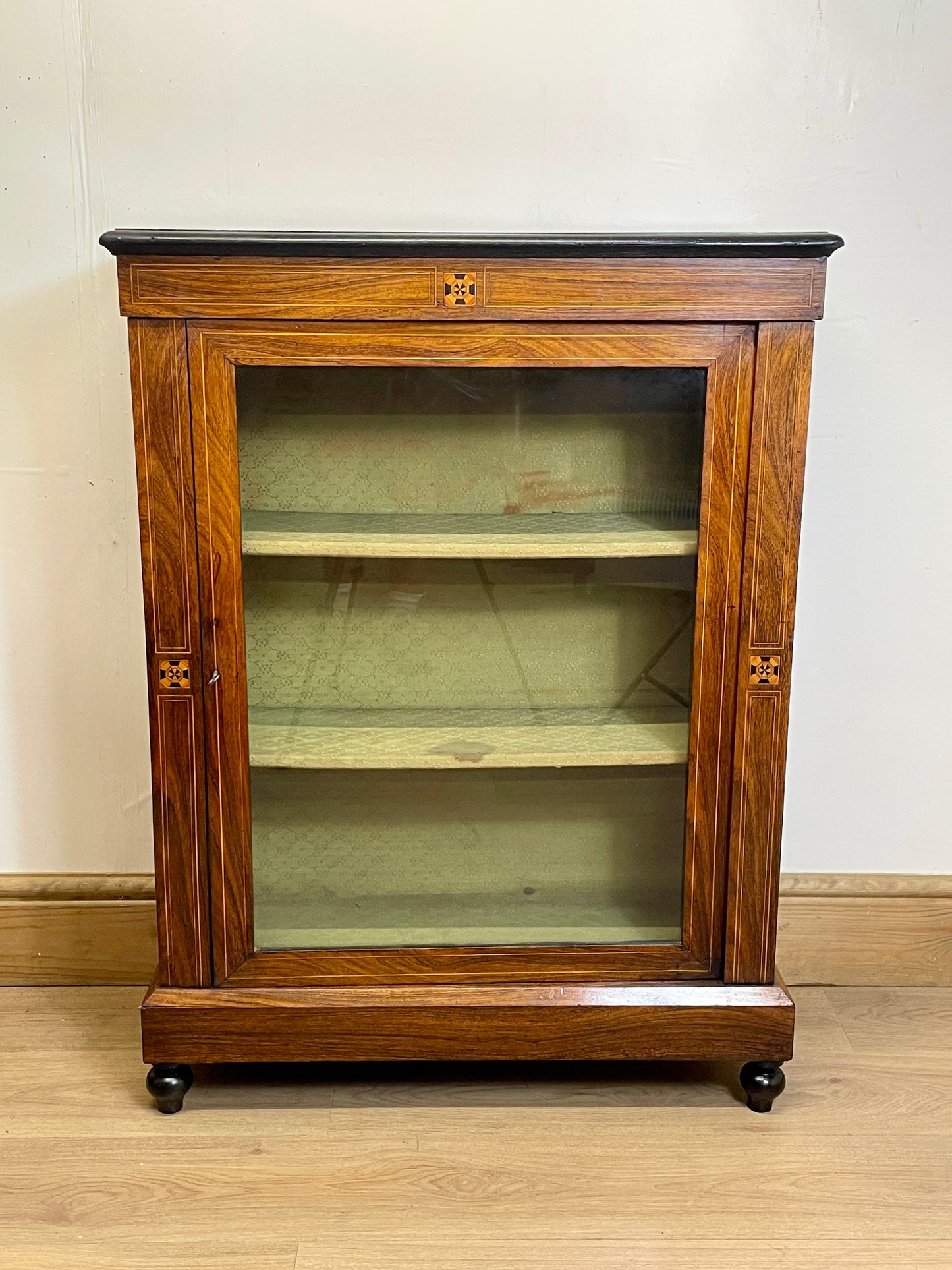 Wooden display cabinet with glass door on a wooden floor.
