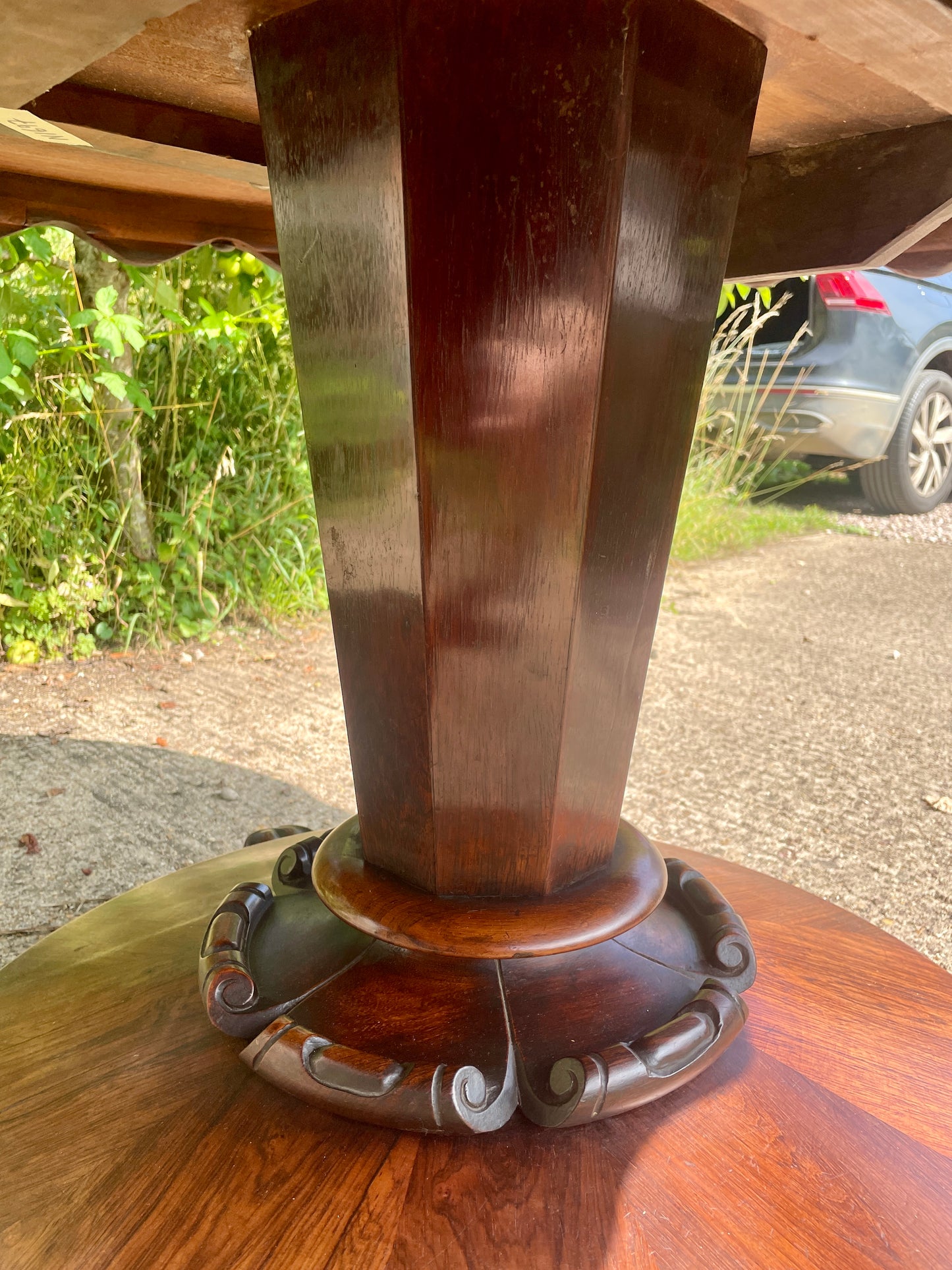 Wooden table base with decorative carvings on a blurred outdoor background