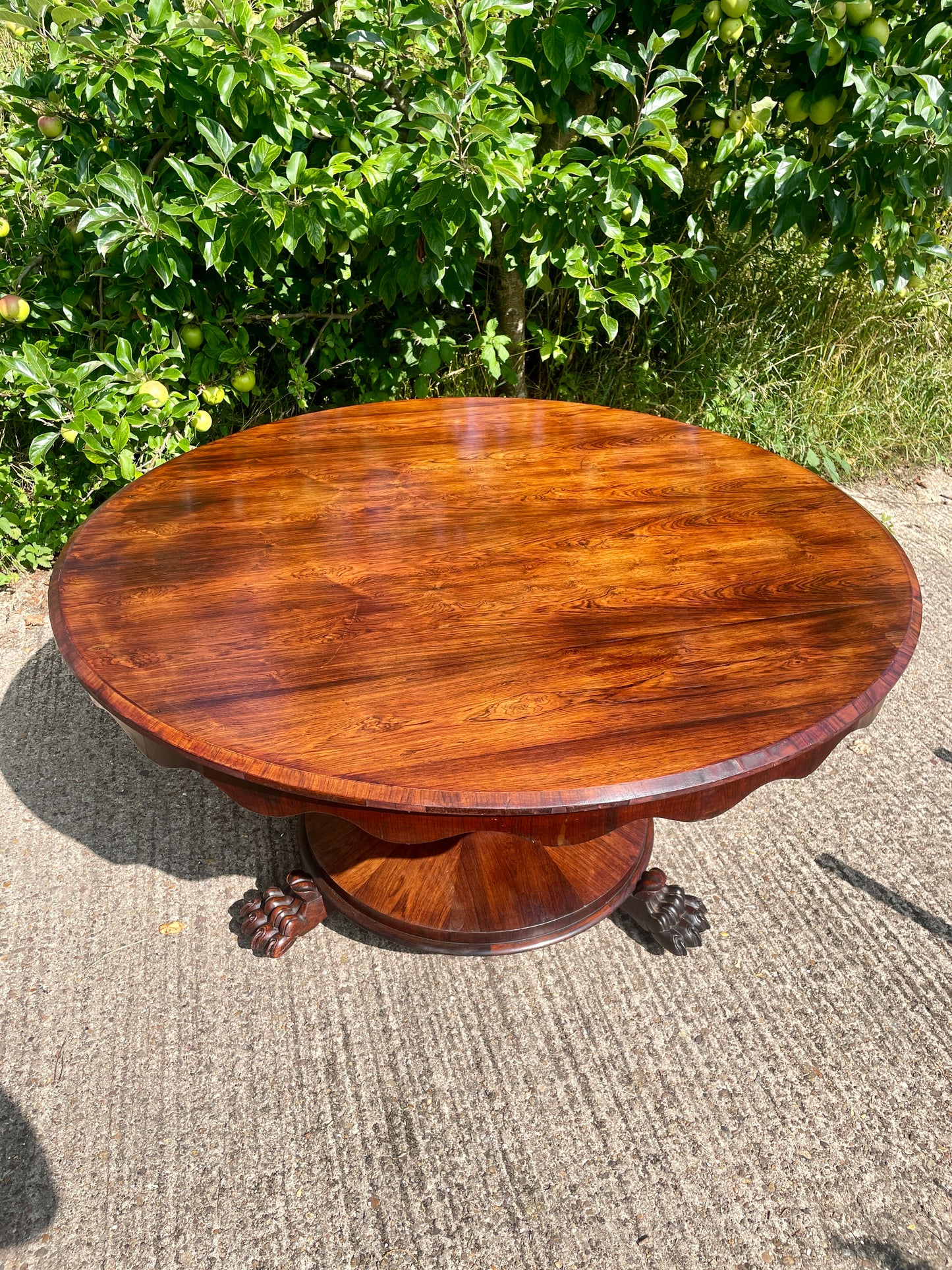 Wooden round table with a textured surface on a concrete ground with greenery in the background