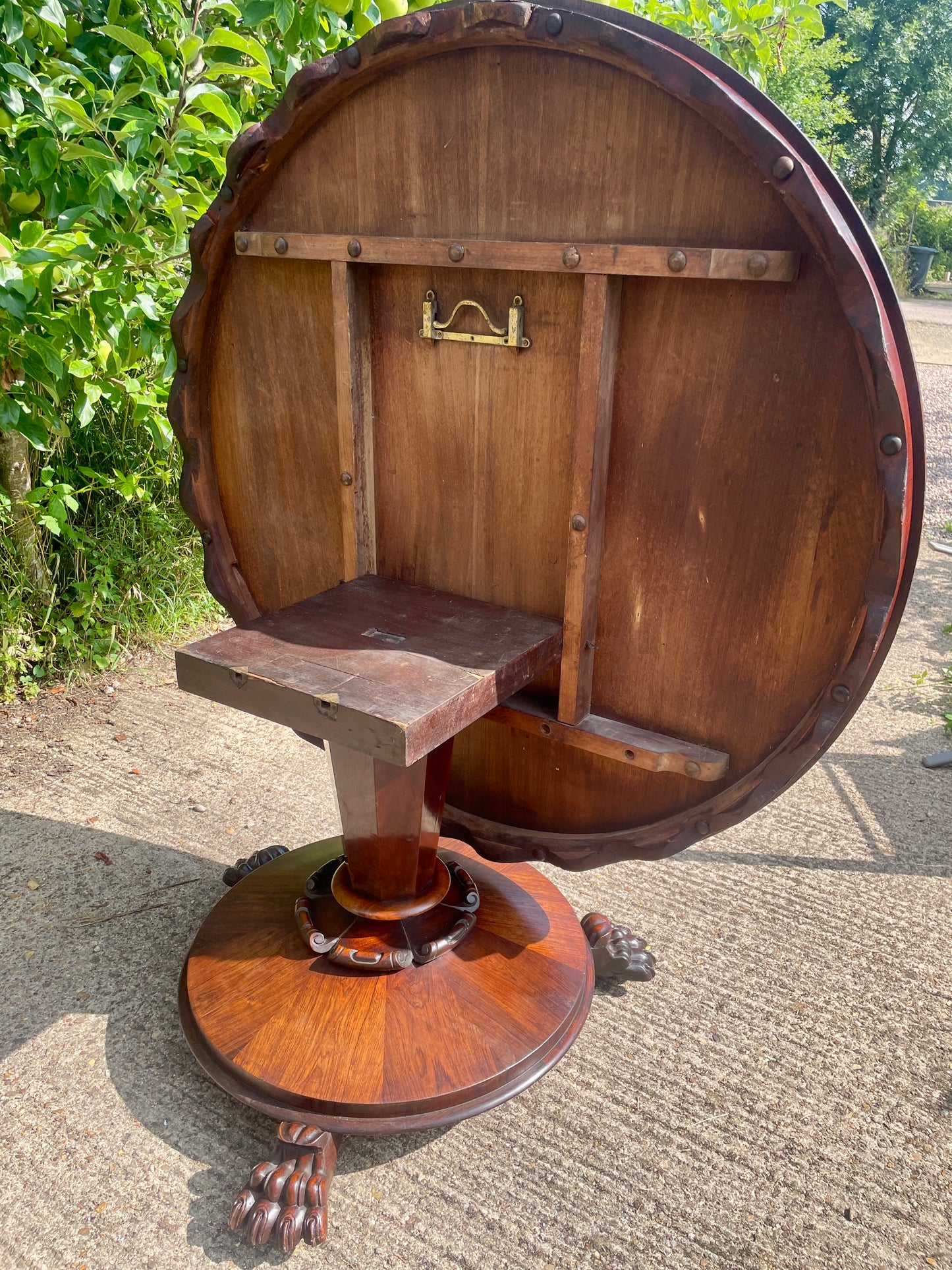 Wooden barrel-shaped table with a seat on a concrete surface with greenery in the background