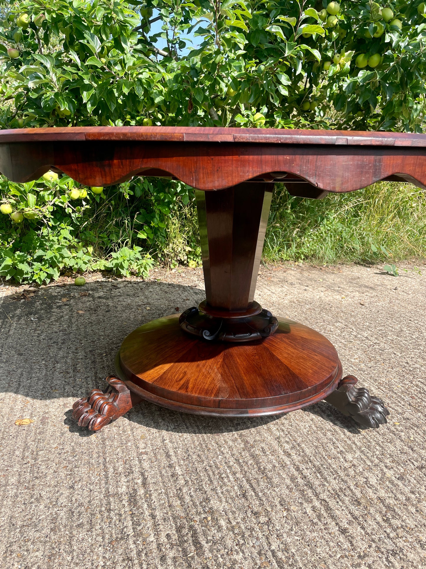 Wooden table with a decorative base on a concrete surface with greenery in the background