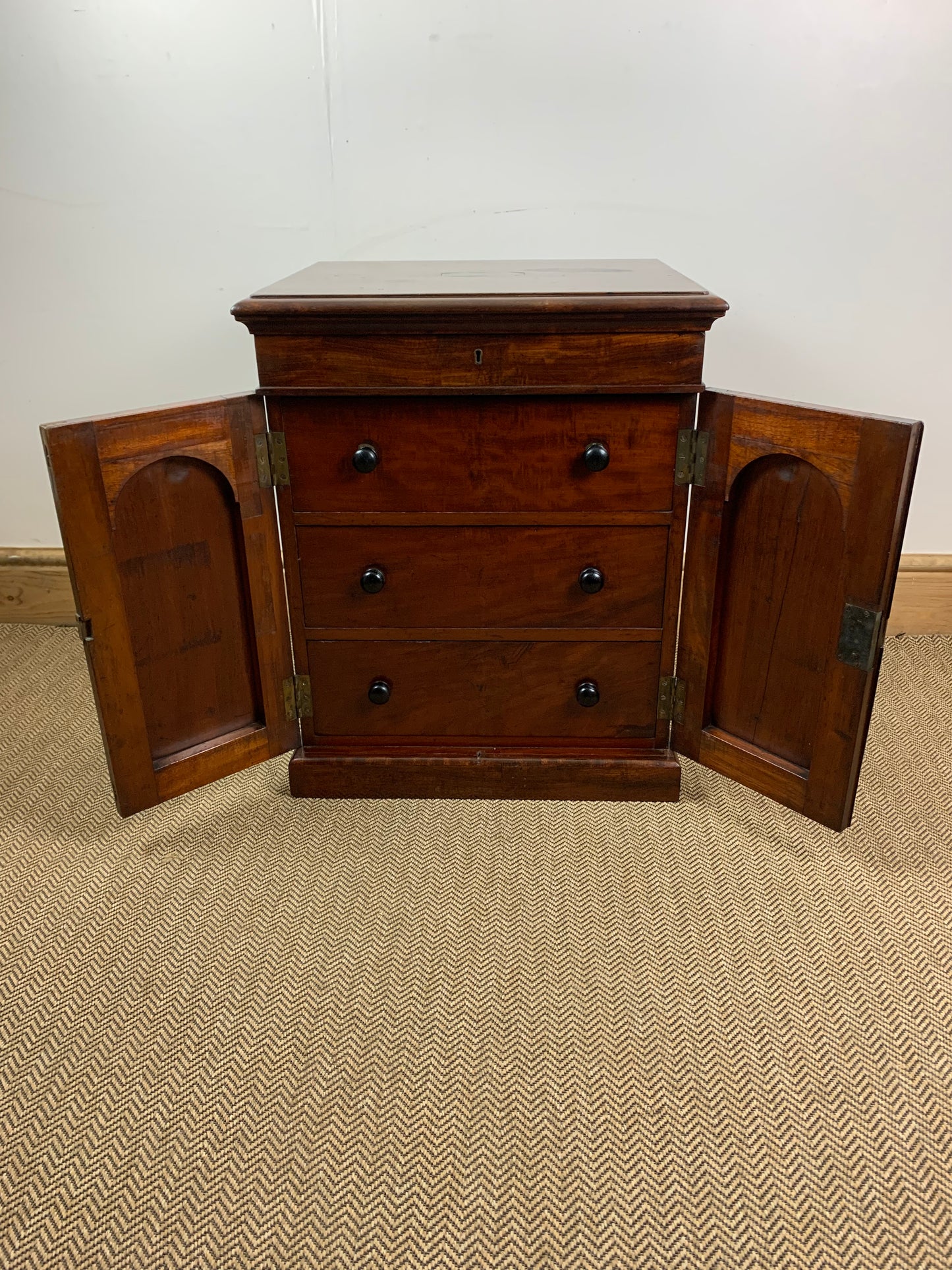An antique mahogany campaign chest with three drawers and two open doors showing the interior, placed on a carpeted floor.