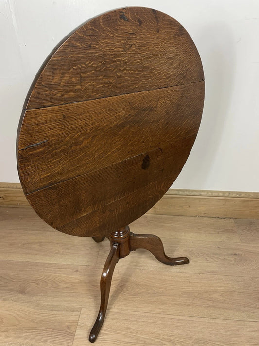 Wooden round table with a single leg on a wooden floor against a white wall