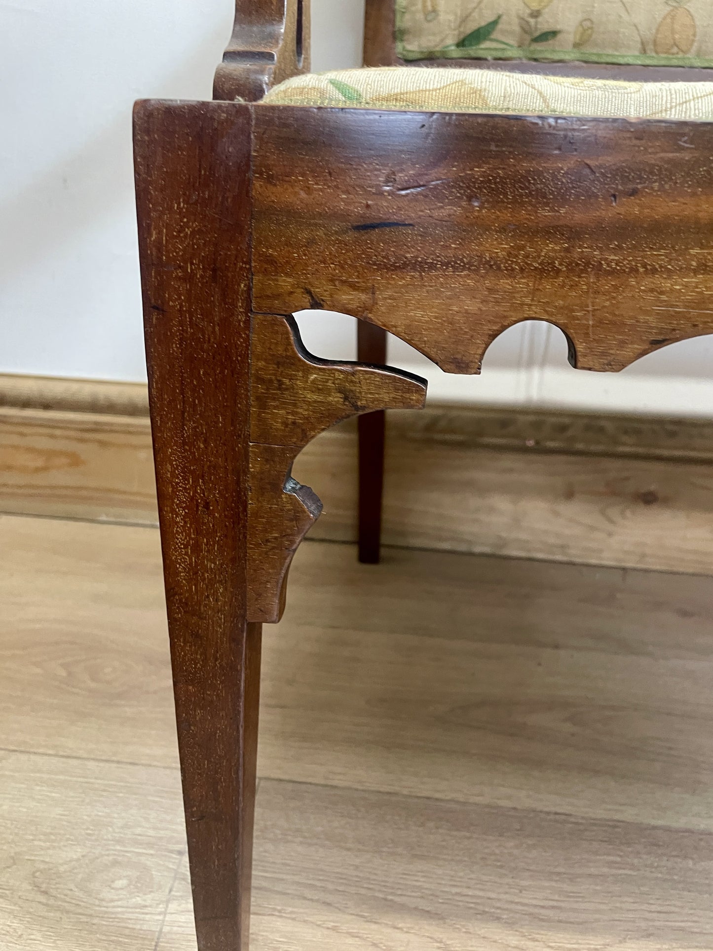 Close-up of a wooden chair leg with a floral cushion on a wooden floor.