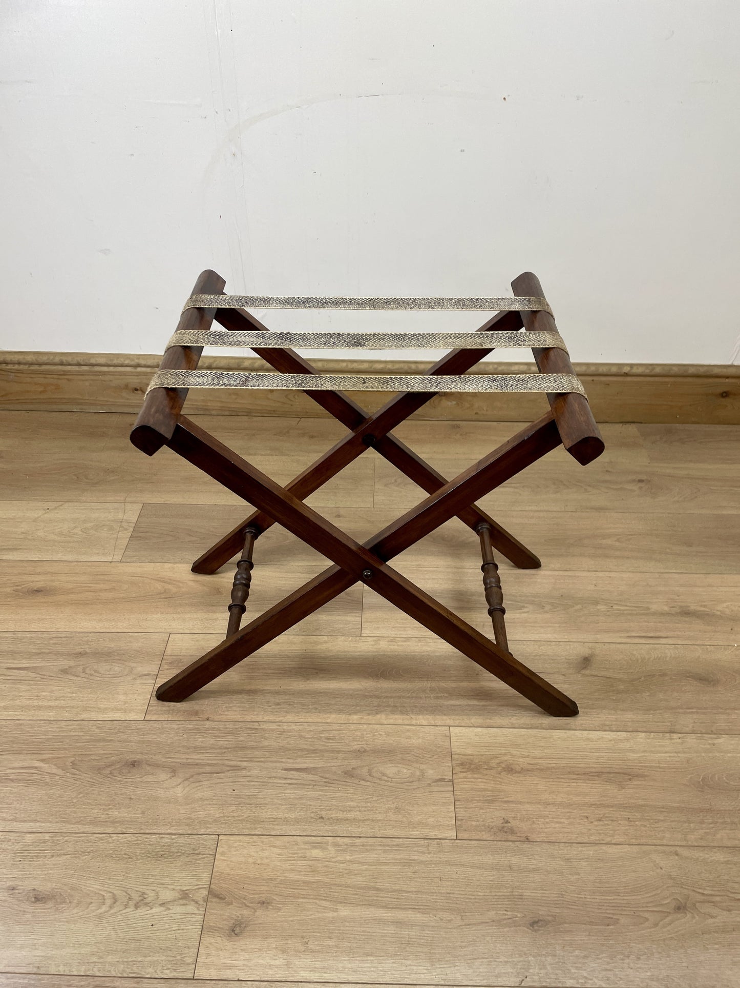 Wooden luggage rack on a wooden floor with a white wall background