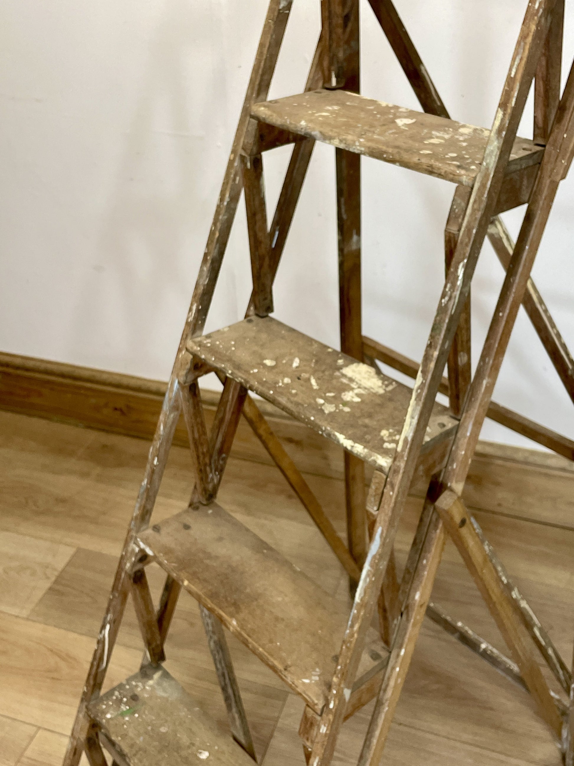 Worn wooden step ladder on a wooden floor against a white wall