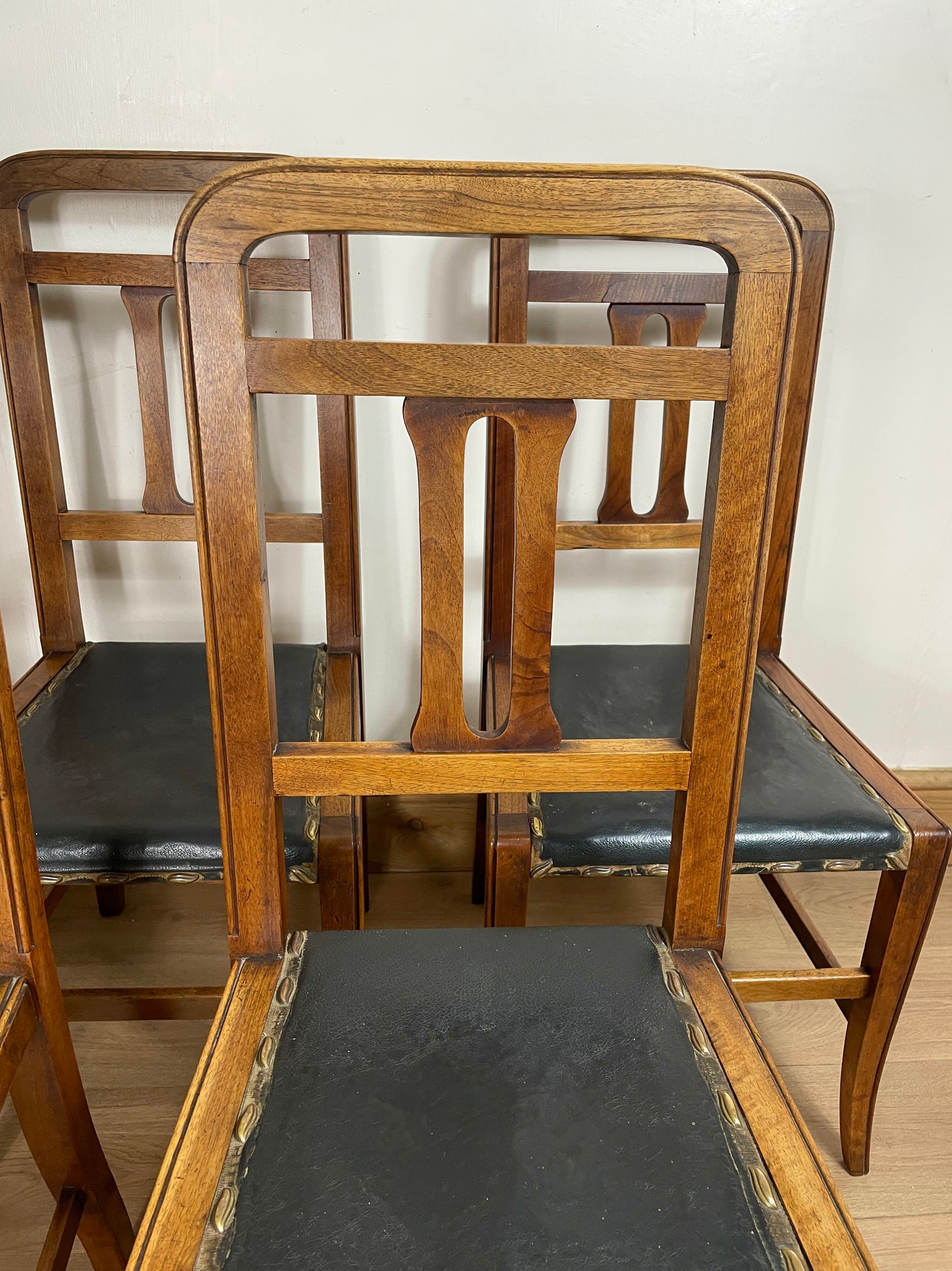 Wooden chairs with black cushioned seats on a wooden floor.