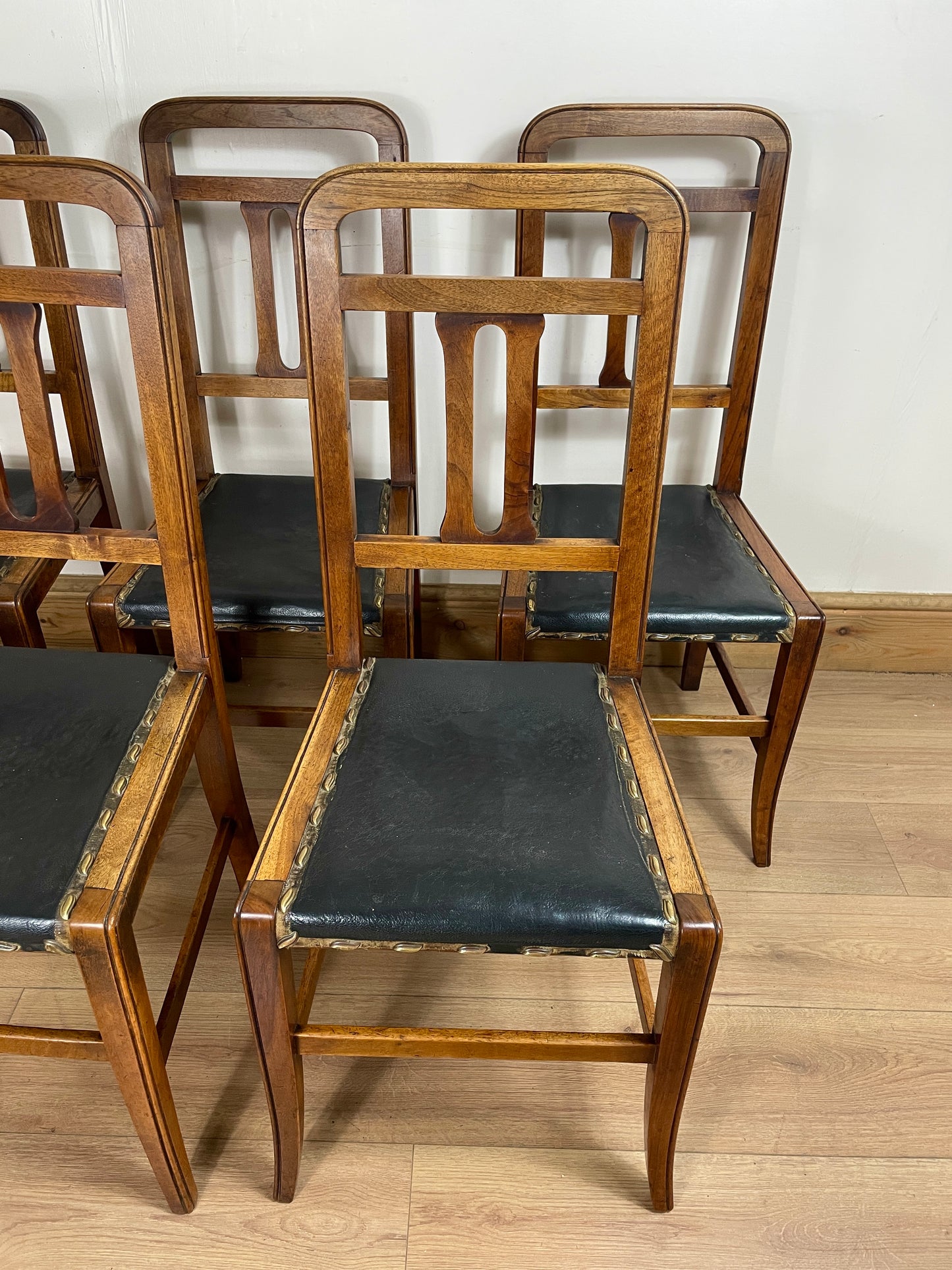 Set of wooden chairs with black seats on a wooden floor.