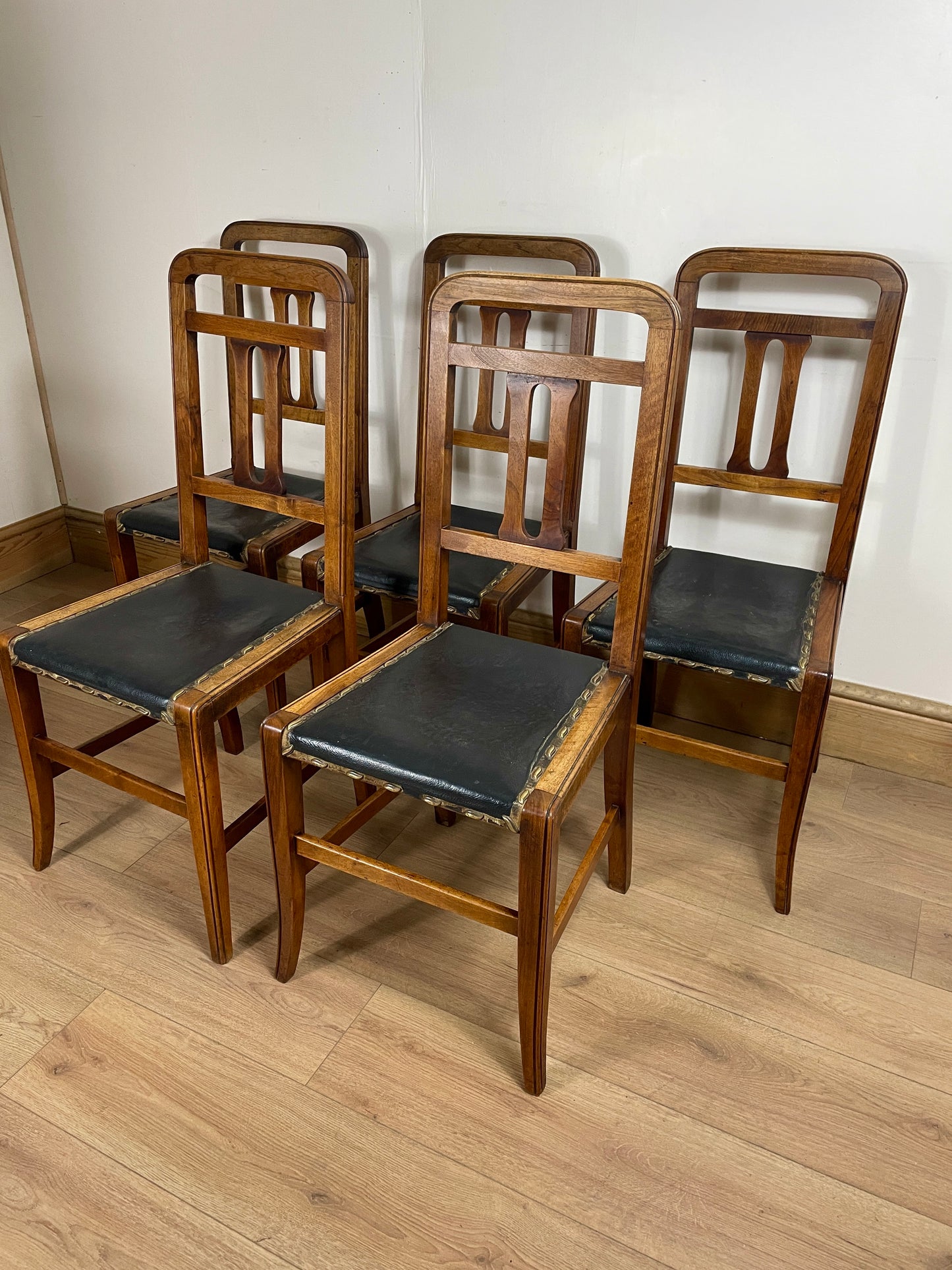 Set of wooden chairs with black seats on a wooden floor.
