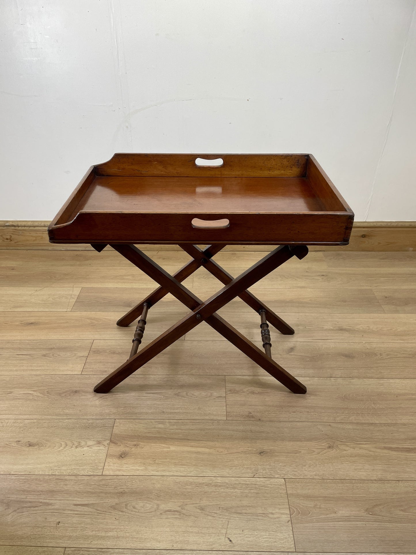 Wooden tray table on a wooden floor with a white wall background