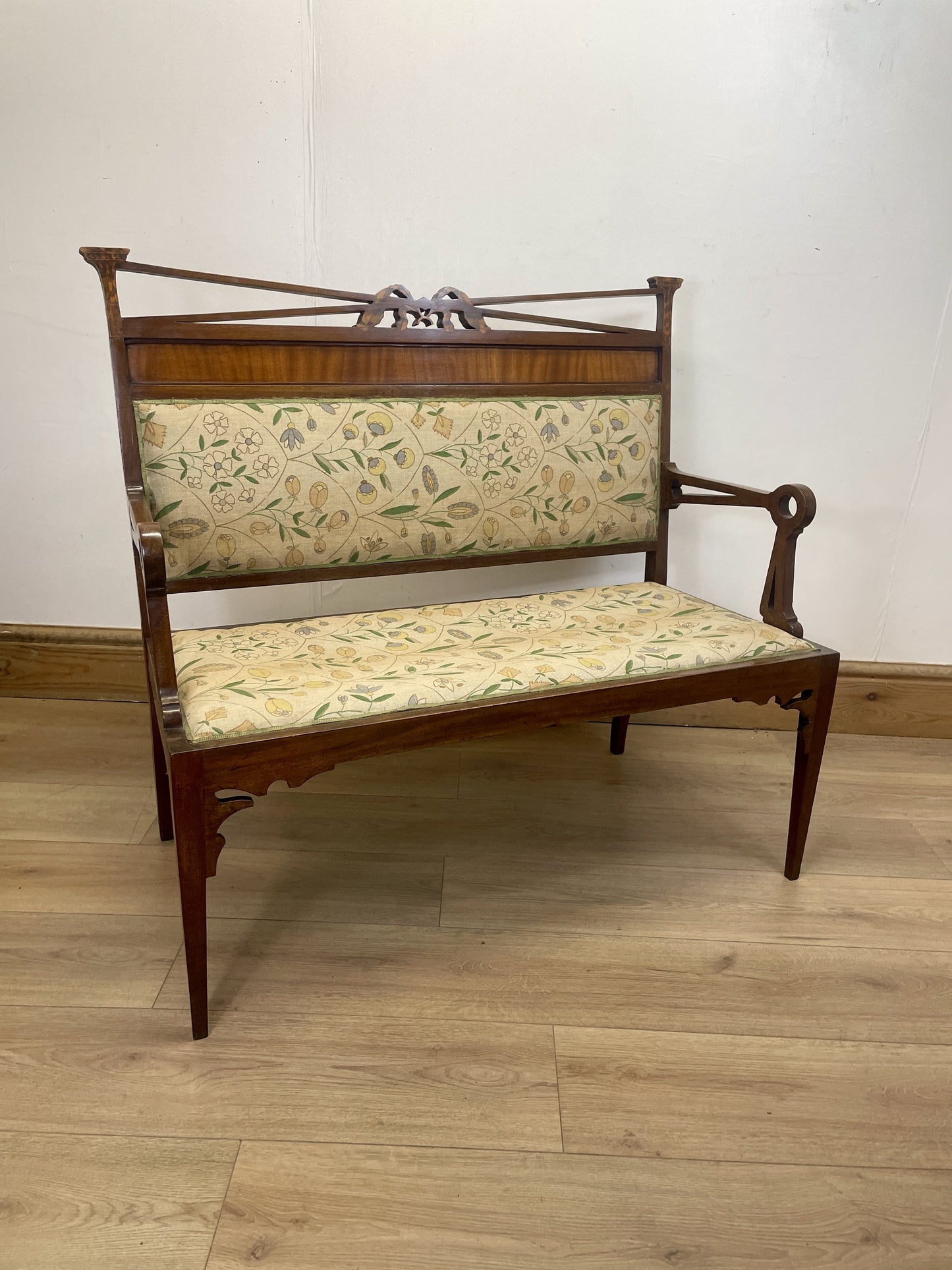 Wooden bench with floral-patterned cushion on a wooden floor against a white wall