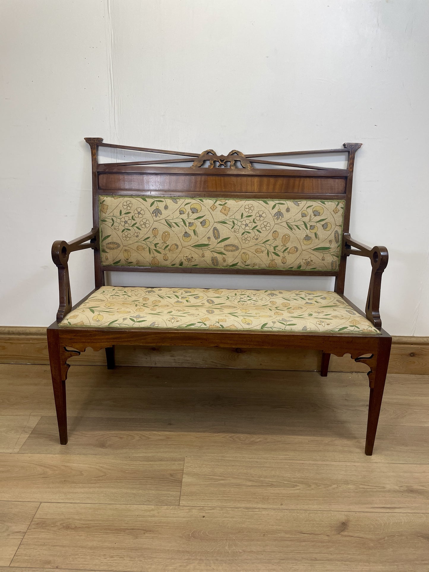 Wooden bench with floral patterned cushion on a wooden floor against a white wall