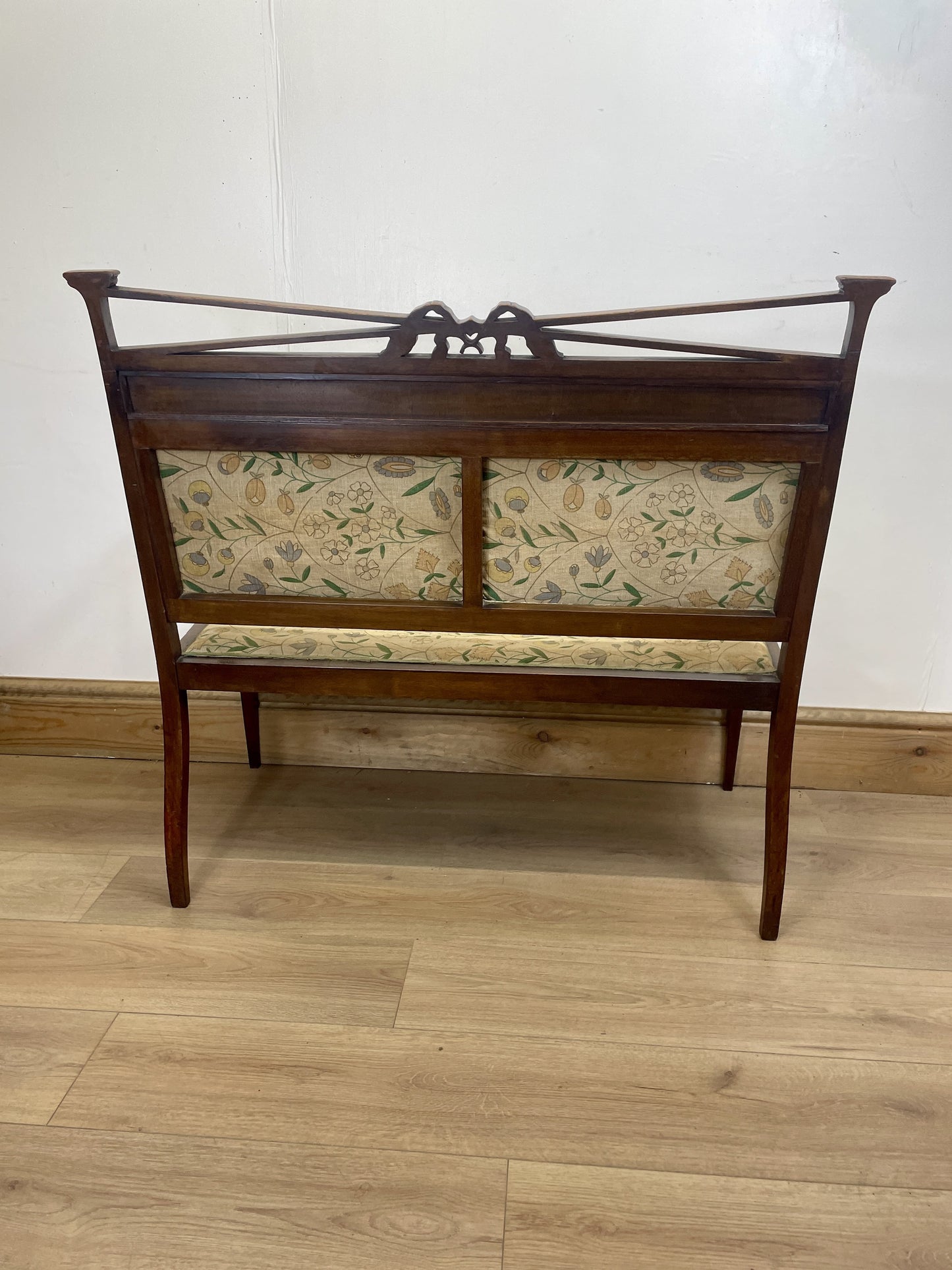 Wooden bench with floral-patterned cushion on a wooden floor against a white wall