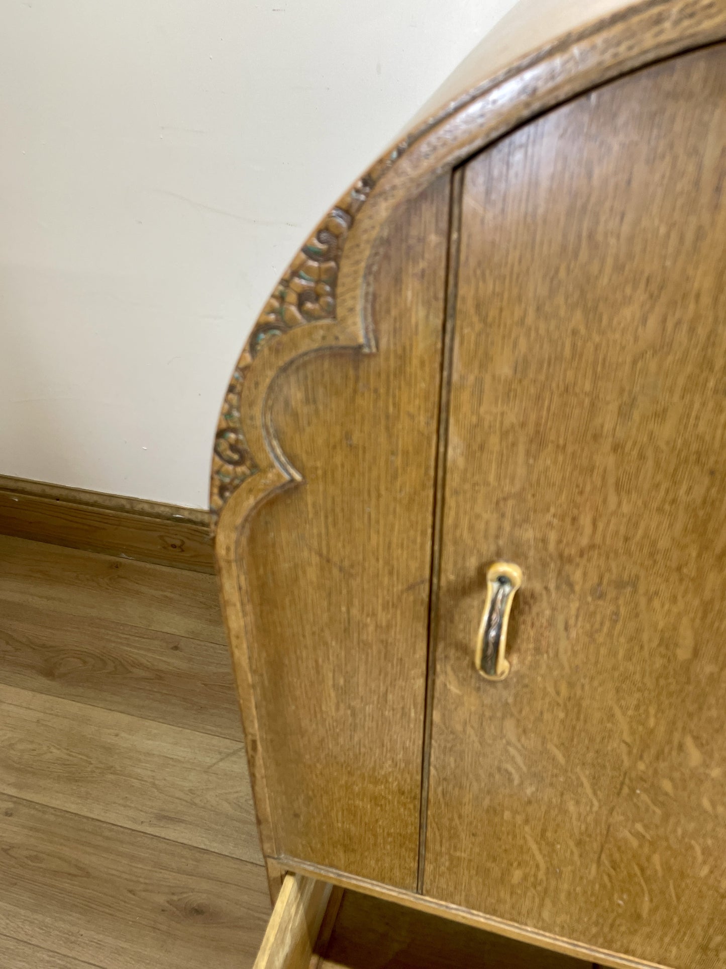 Wooden cabinet with curved top and gold handle on a wooden floor.