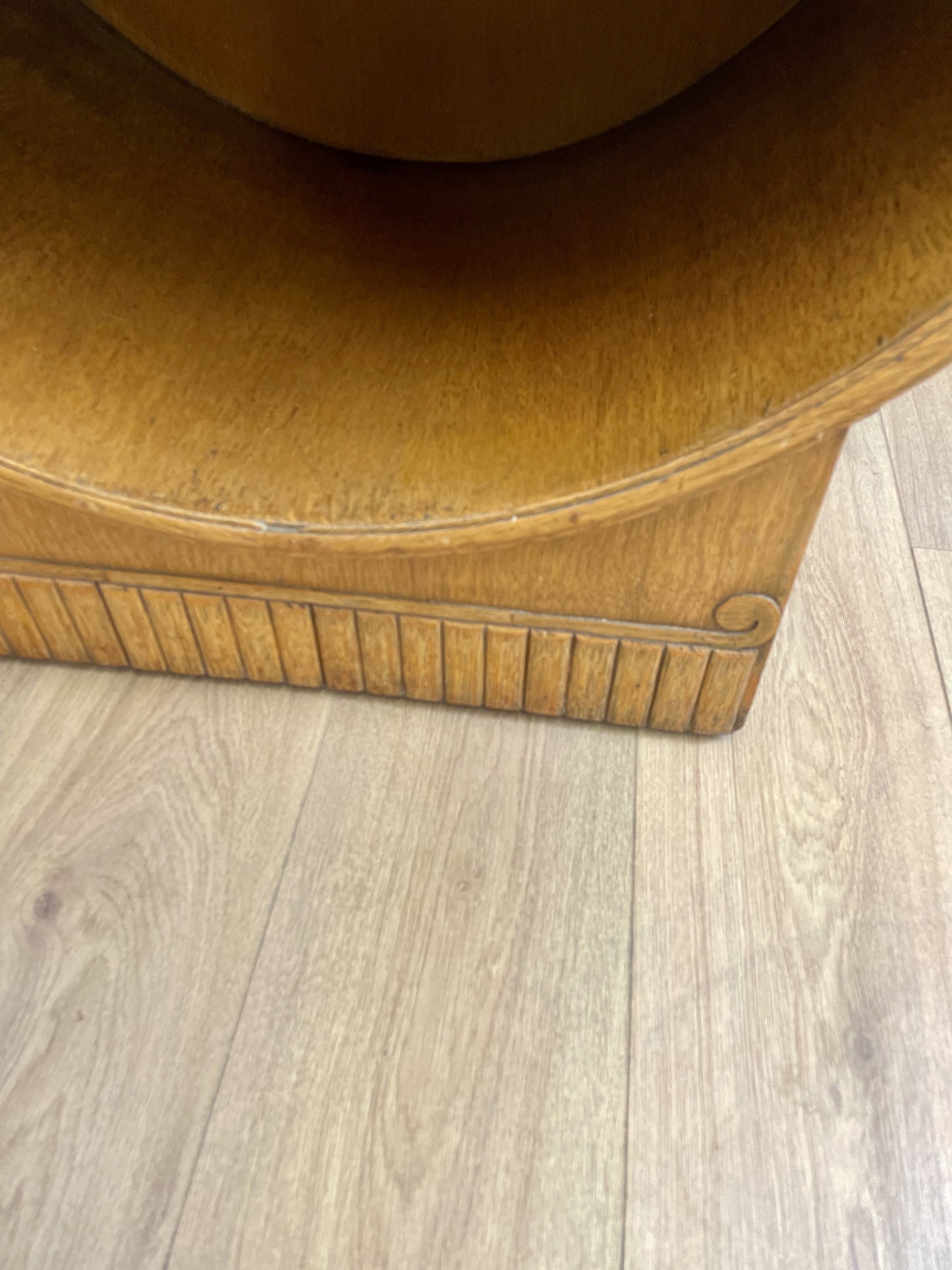 Close-up of a brown leather armchair corner on a wooden floor.