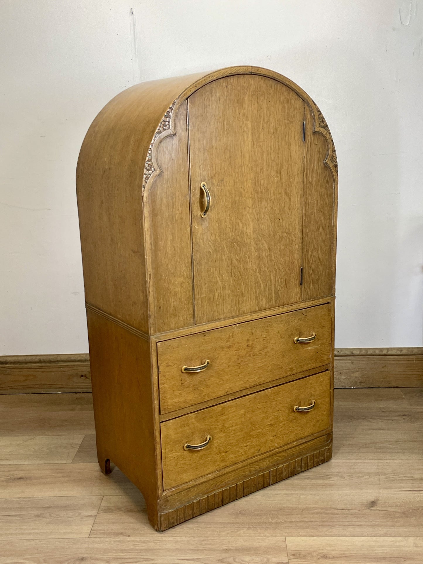 Wooden armoire with curved top and two drawers on a wooden floor.