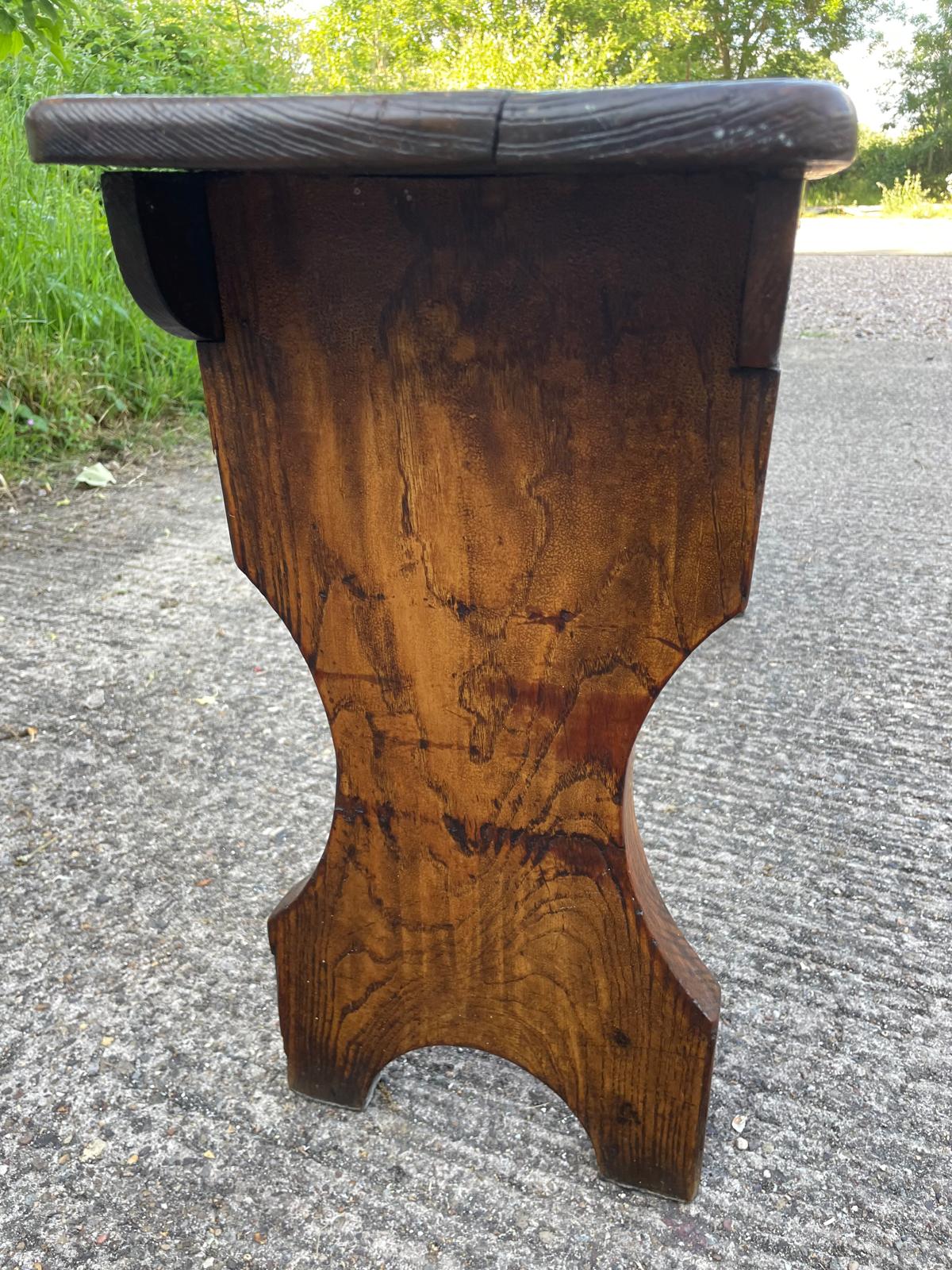 Wooden stool with a curved design on a concrete surface with grass in the background
