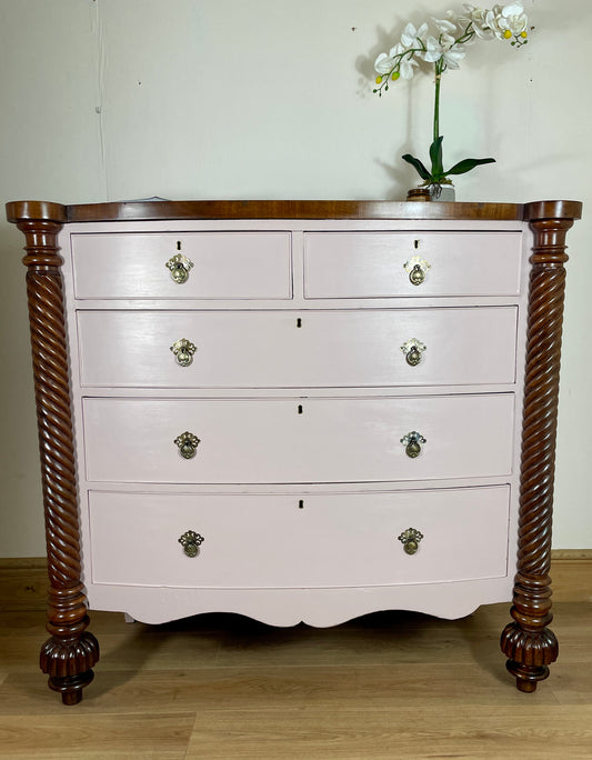 Antique Victorian pink chest of drawers with painted bow front and ornate metal handles.