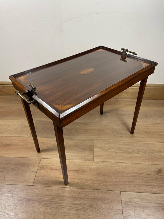 An Edwardian folding butler's table made of mahogany, with visible signs of wear and restoration, standing on a wooden floor.