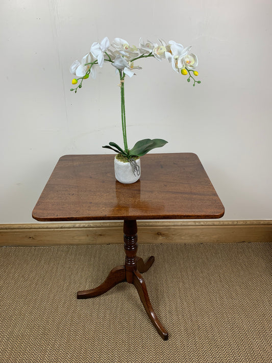 A Georgian mahogany tilt-top table with a central pedestal leg, polished finish, and a floral arrangement on top.