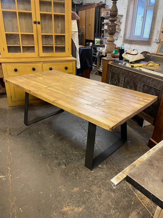 A large rectangular pine wood dining table with a metal base, designed to seat 10 people, in a room with various furniture.