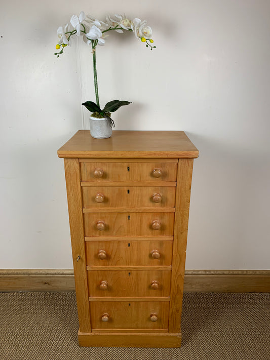 A Victorian Pine Cupboard with multiple drawers, presented in a room with a vase of flowers on top.