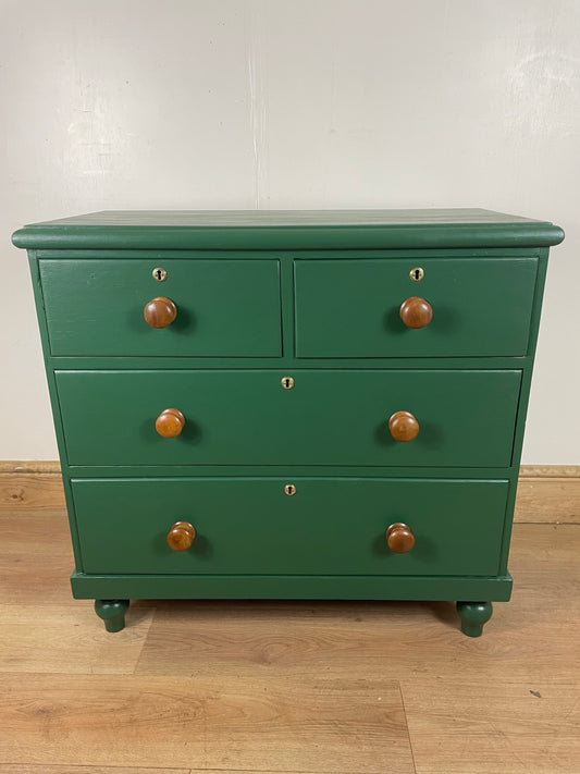 A green painted Victorian chest of drawers with five drawers, original handles, and escutcheons, on a wooden floor.