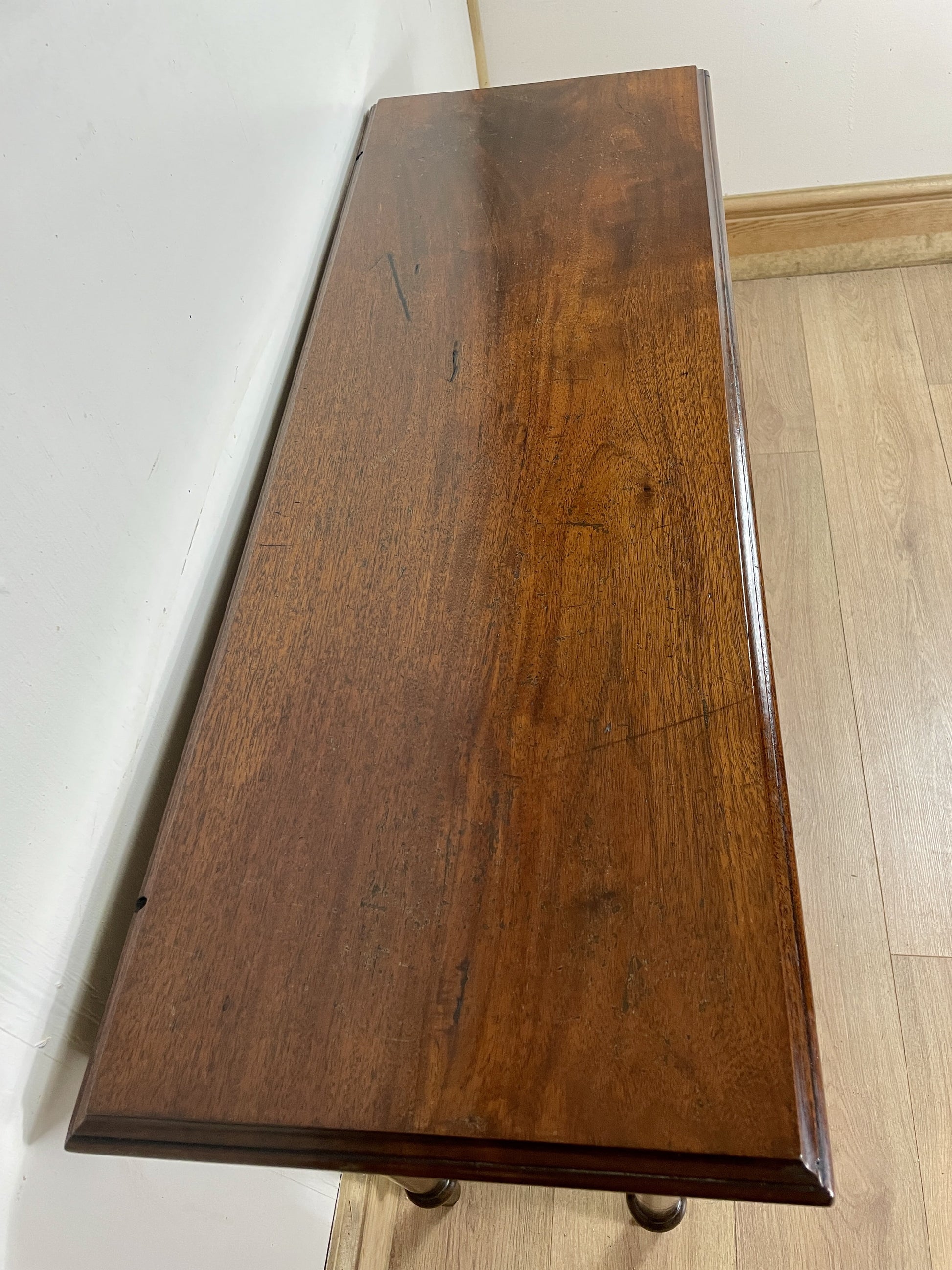 Wooden table top with a dark brown finish on a light wooden floor.