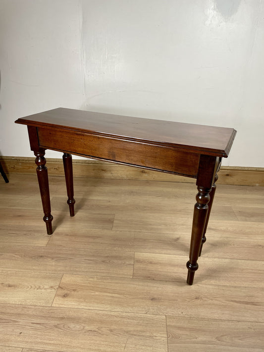 Wooden table with a dark finish on a wooden floor against a white wall