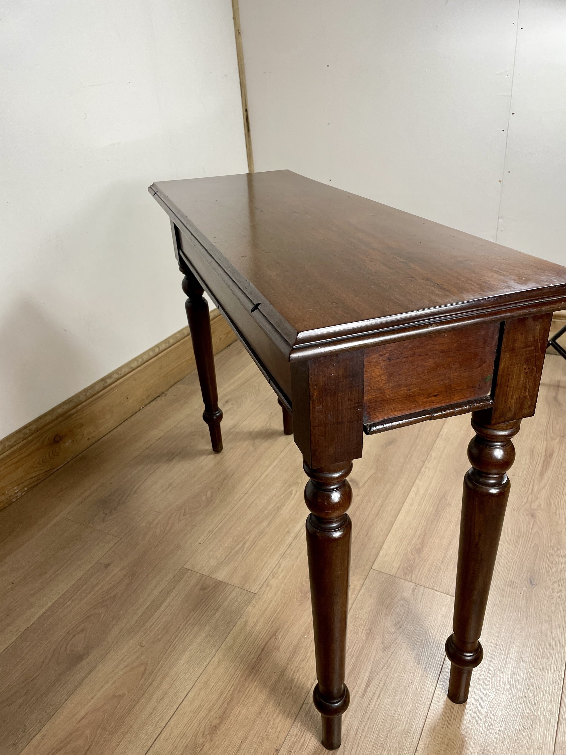 Wooden table with a dark finish on a wooden floor against a white wall.