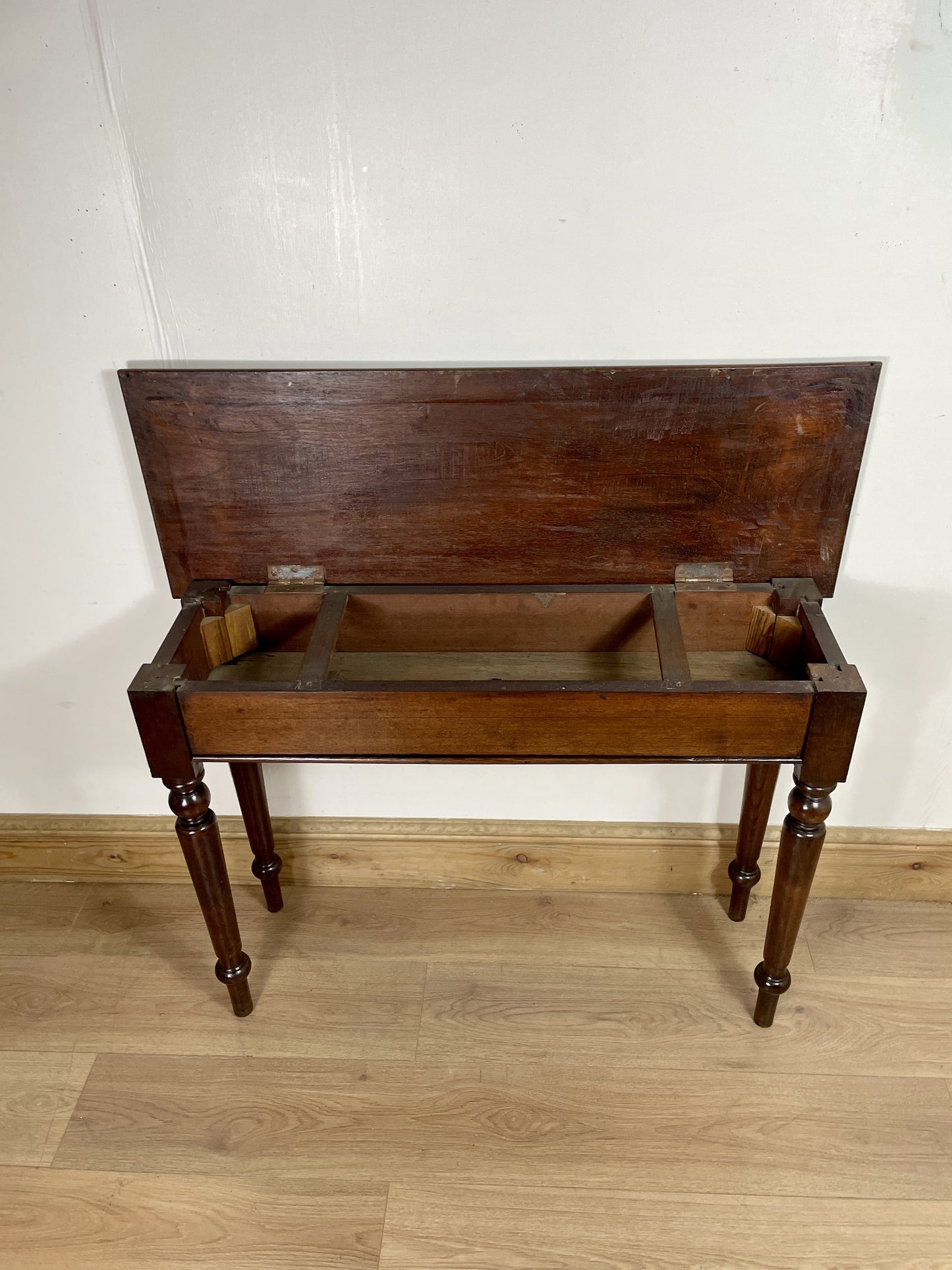 Wooden washstand with a rectangular basin on a wooden floor against a white wall.