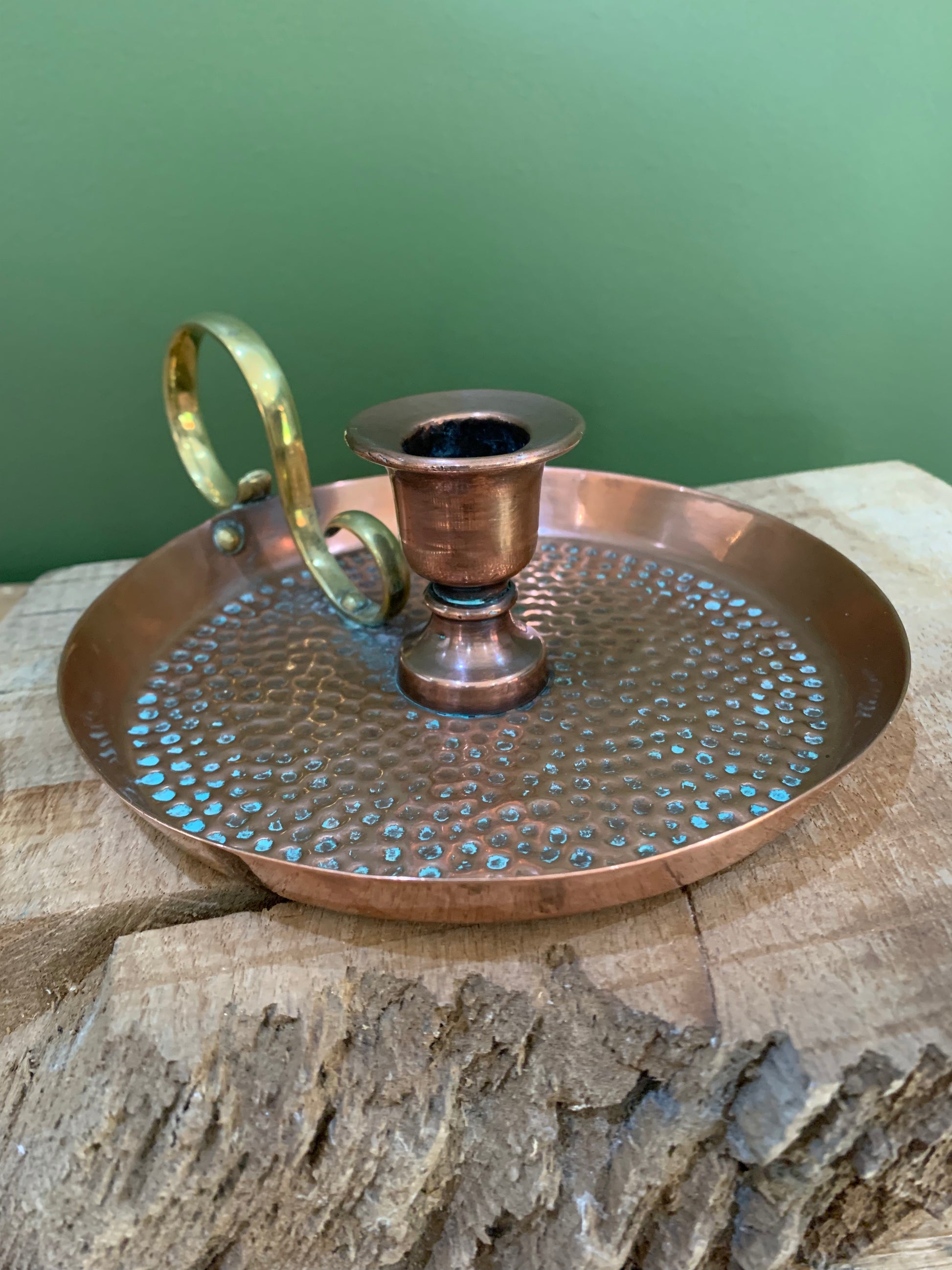 Antique copper and brass candle holder with a hammered texture, displayed on a wooden surface.