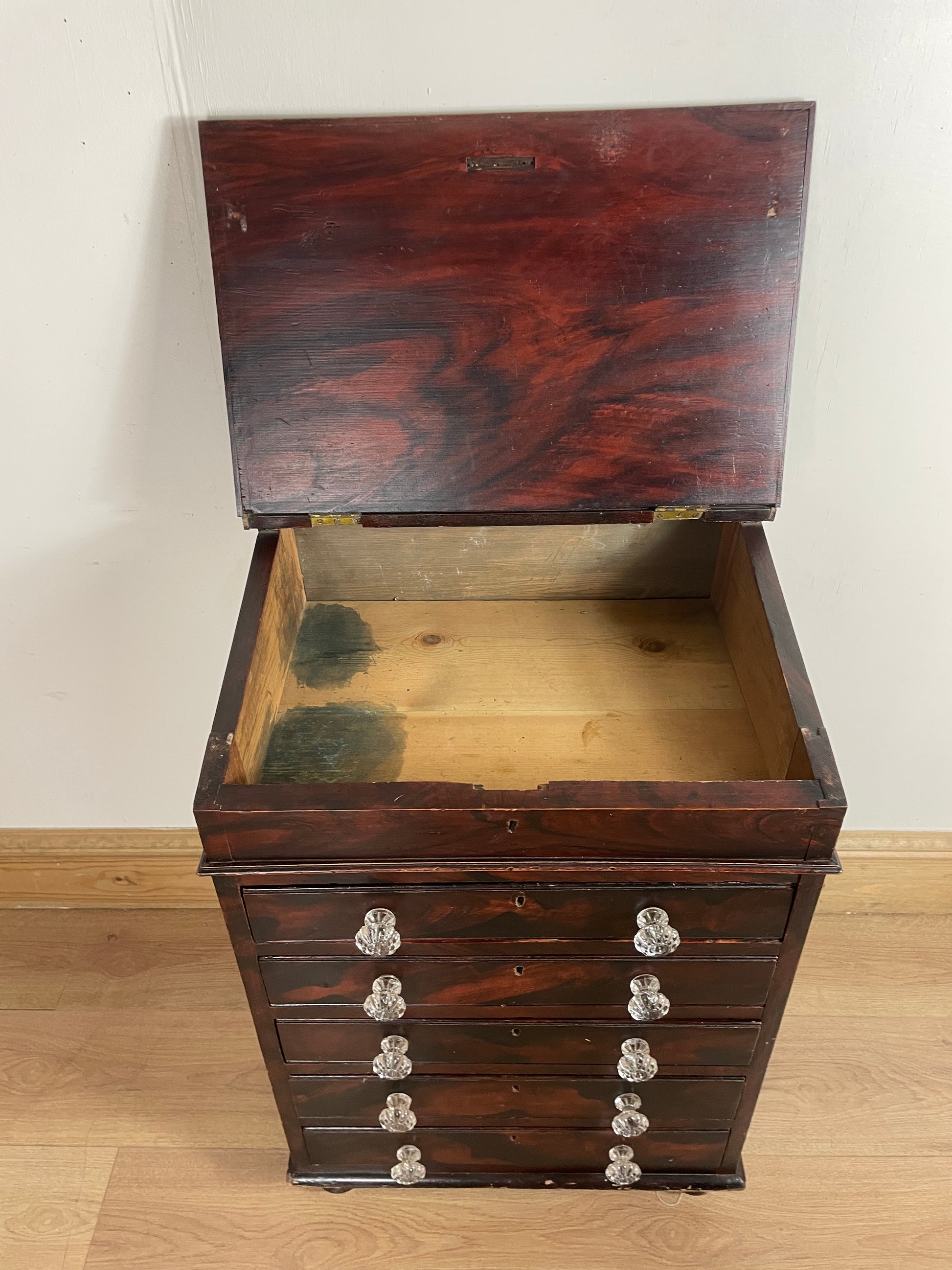 Wooden box with a textured surface, open to reveal greenery inside, on a light wooden floor.