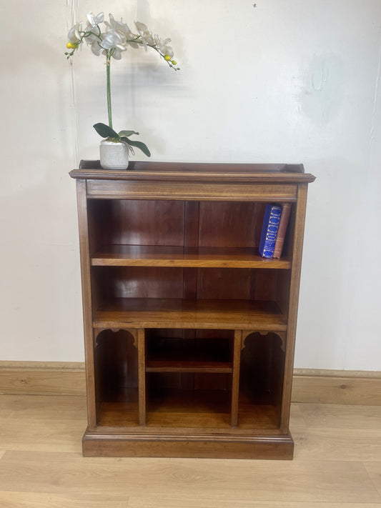 Wooden bookshelf with a vase of flowers on top against a white wall.