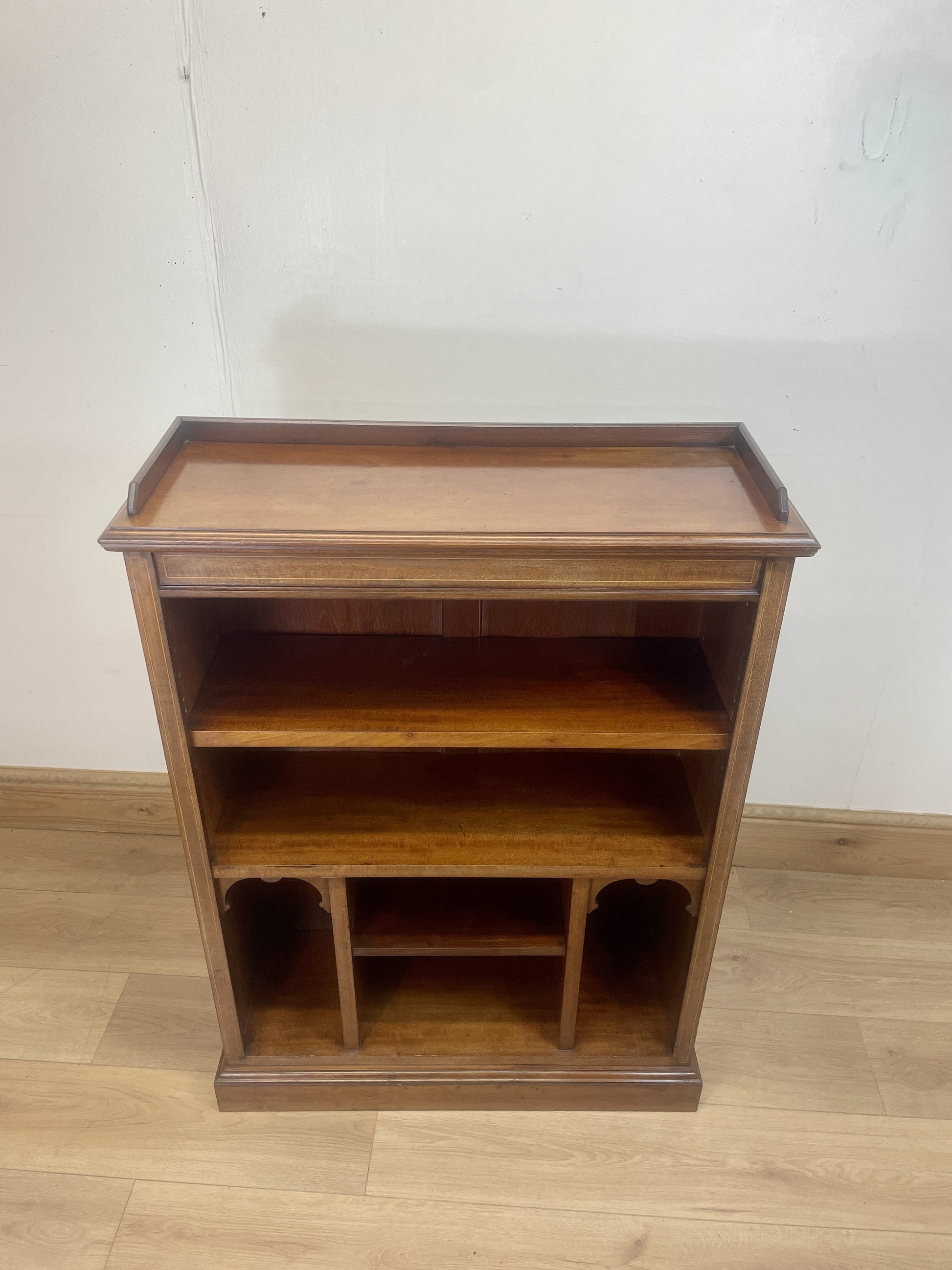 Wooden bookshelf with three shelves on a wooden floor against a white wall