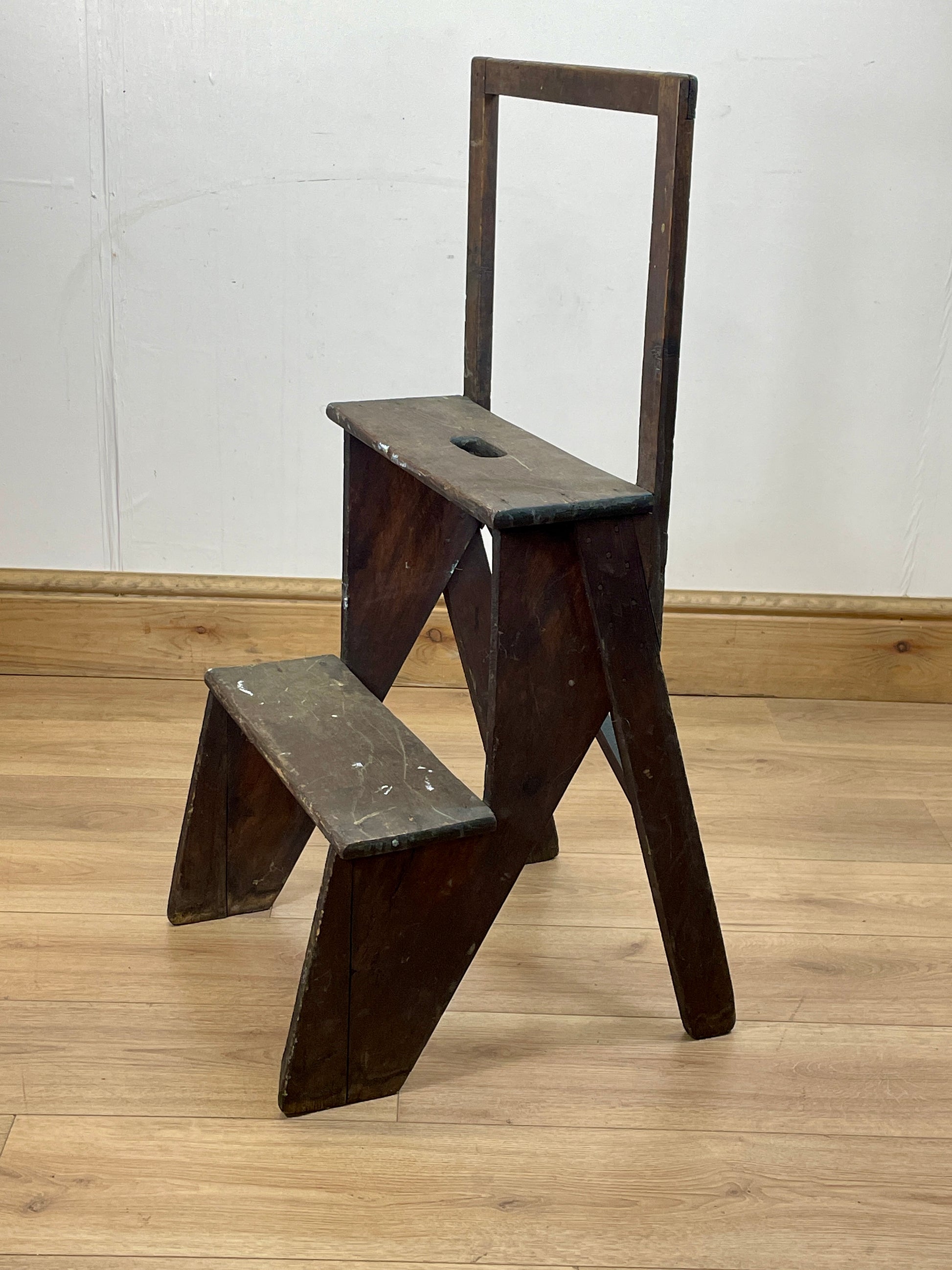 Wooden step stool with a backrest on a wooden floor against a white wall