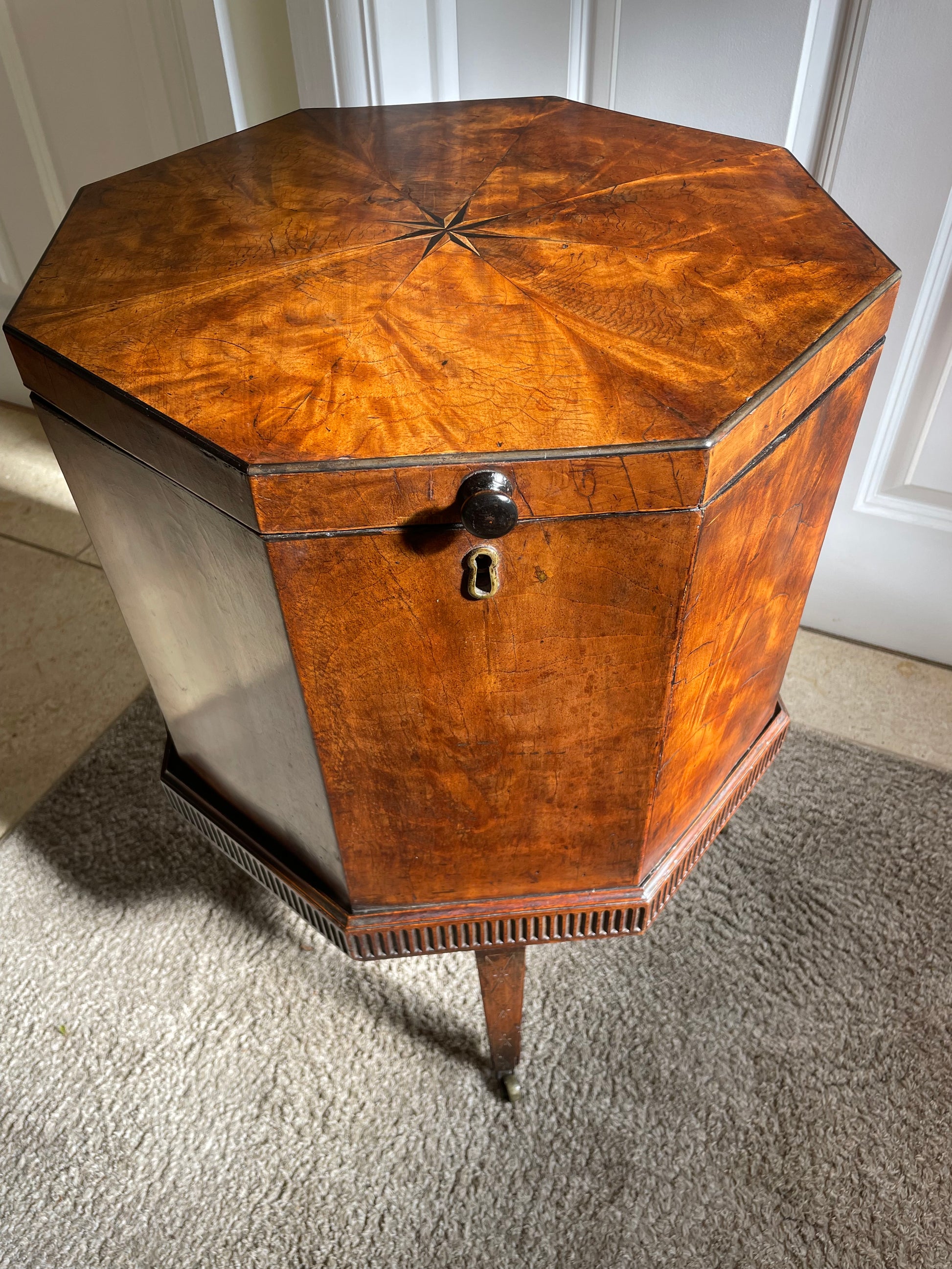 A Georgian burr walnut wine cooler with a star motif inlaid in the center, on original castors, in a room setting.