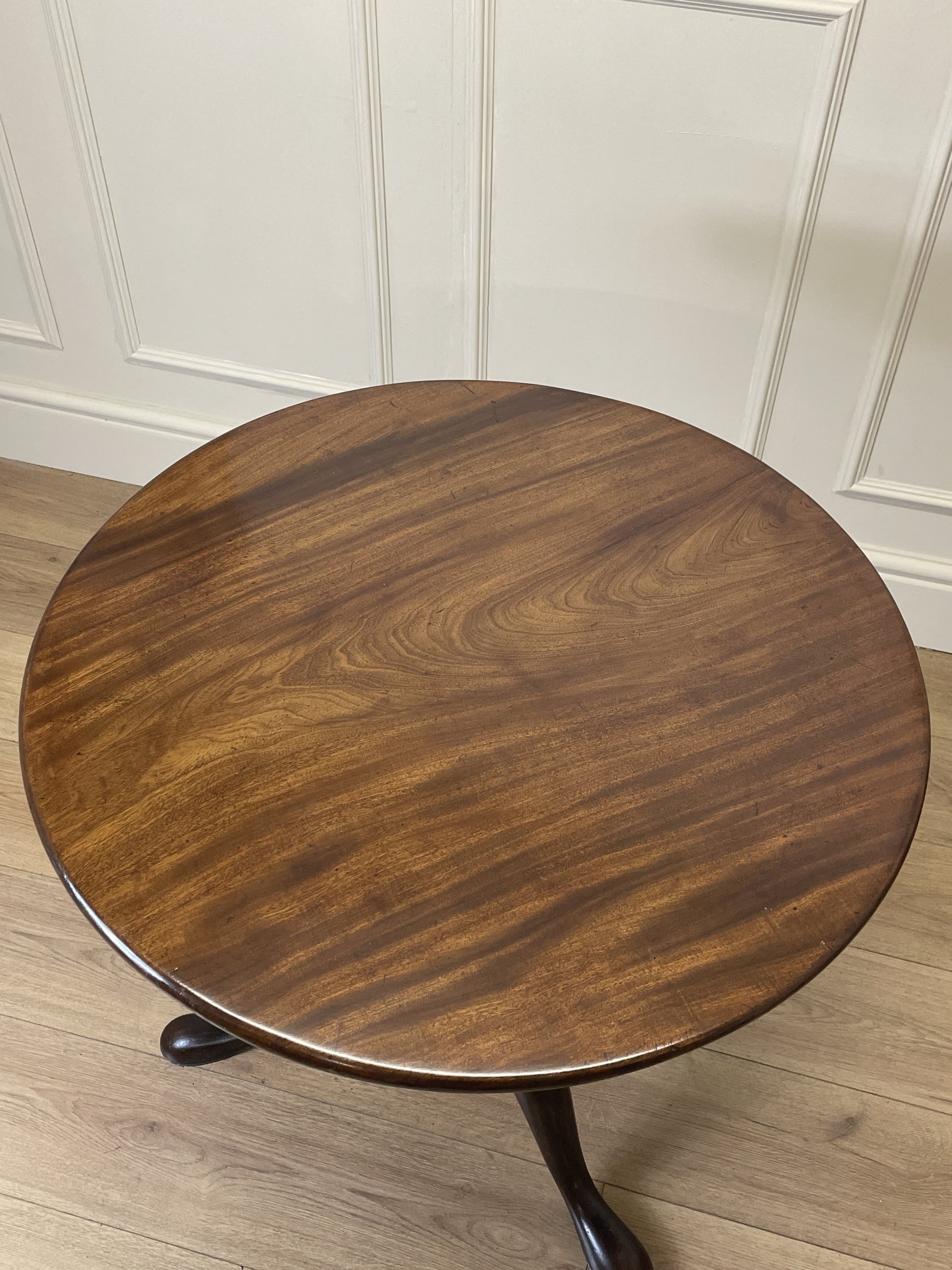 Round wooden table with a dark finish on a light wood floor against a white paneled wall.