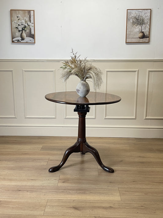 Round wooden table with a vase of flowers in a room with panelled walls and wooden flooring.