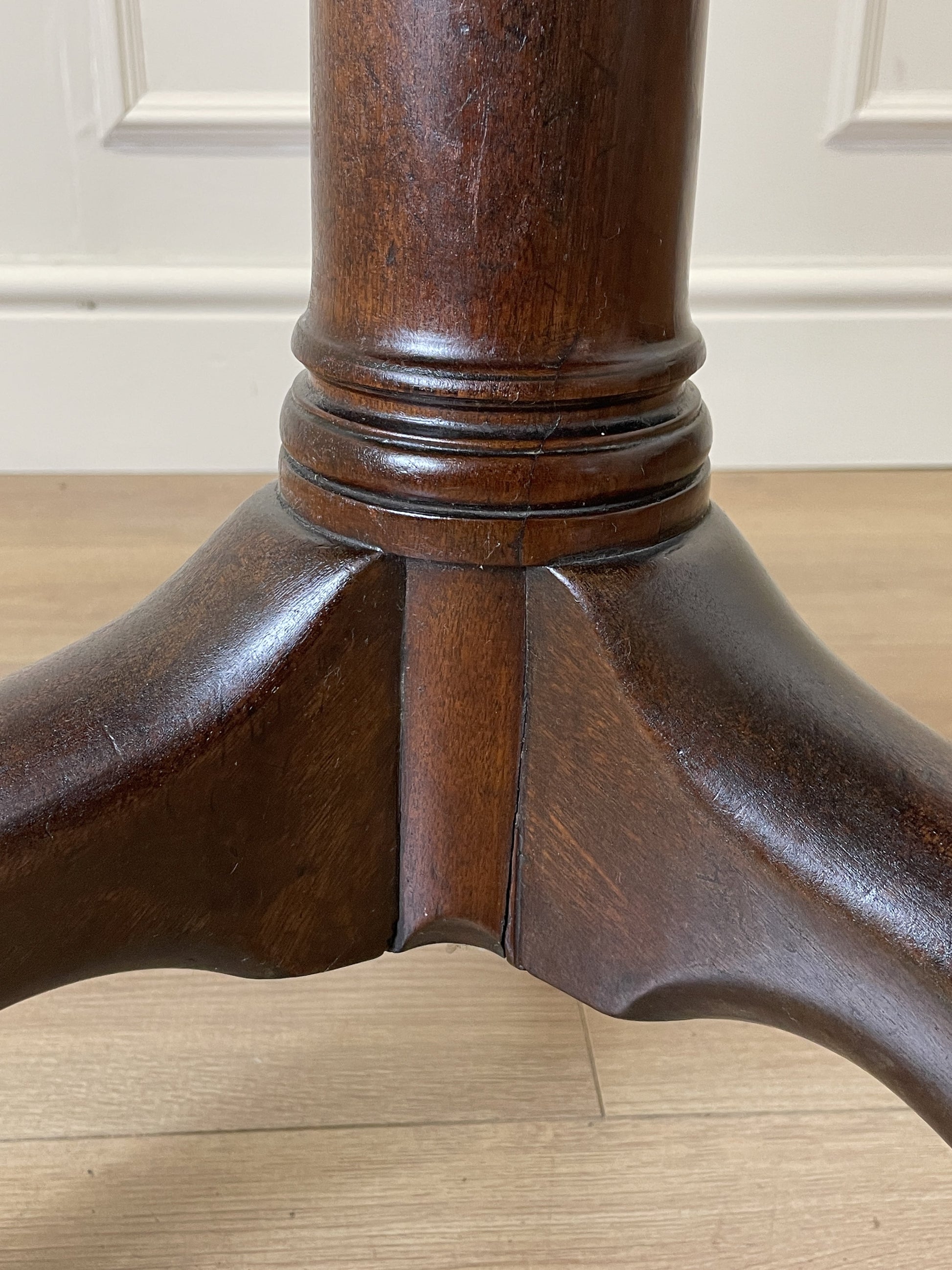 Close-up of a wooden pedestal base on a wooden floor.