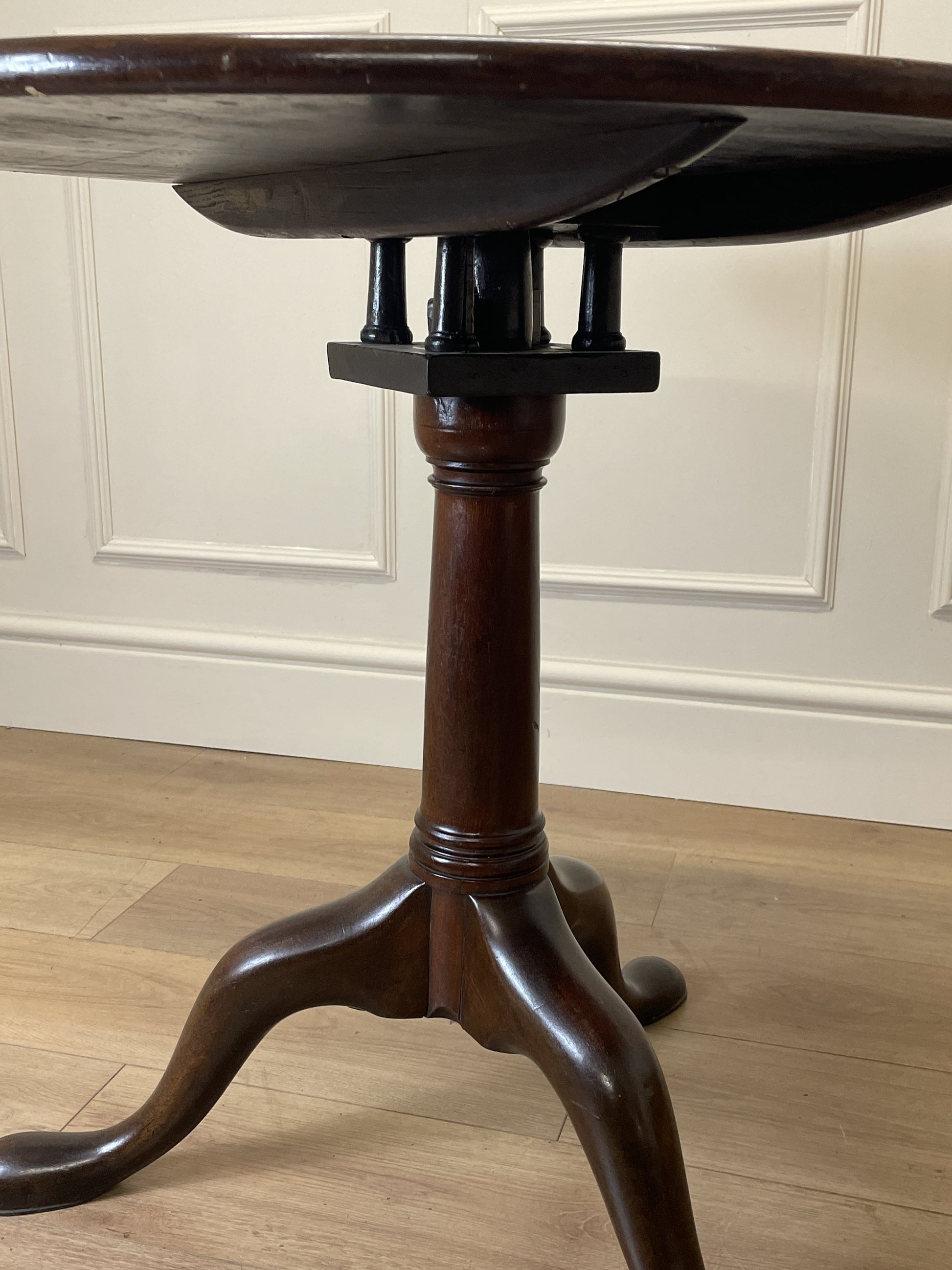 Wooden pedestal table against a white paneled wall.