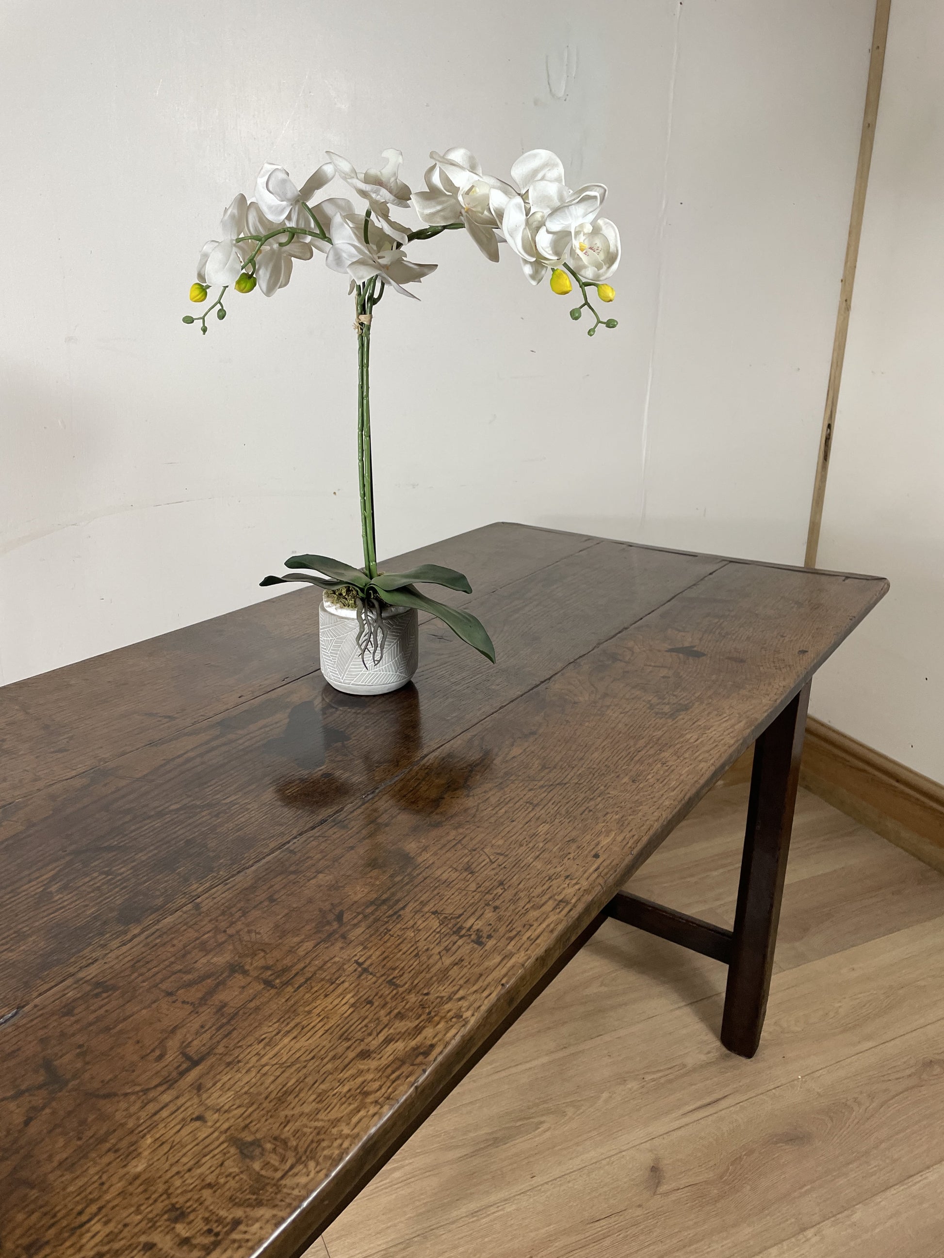 Floral arrangement in a pot on a wooden table against a plain wall.