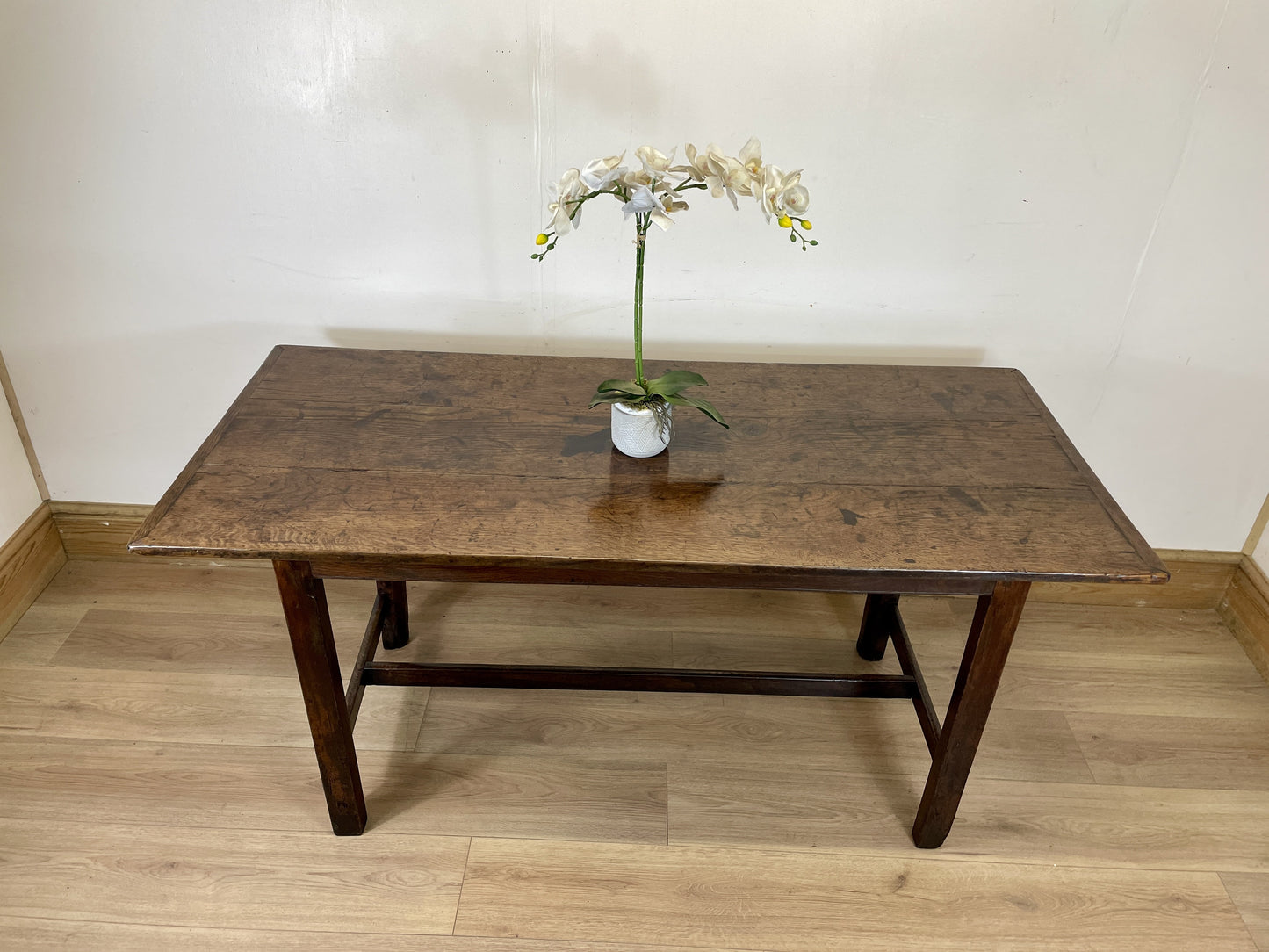 Wooden table with a vase of flowers on a wooden floor against a white wall